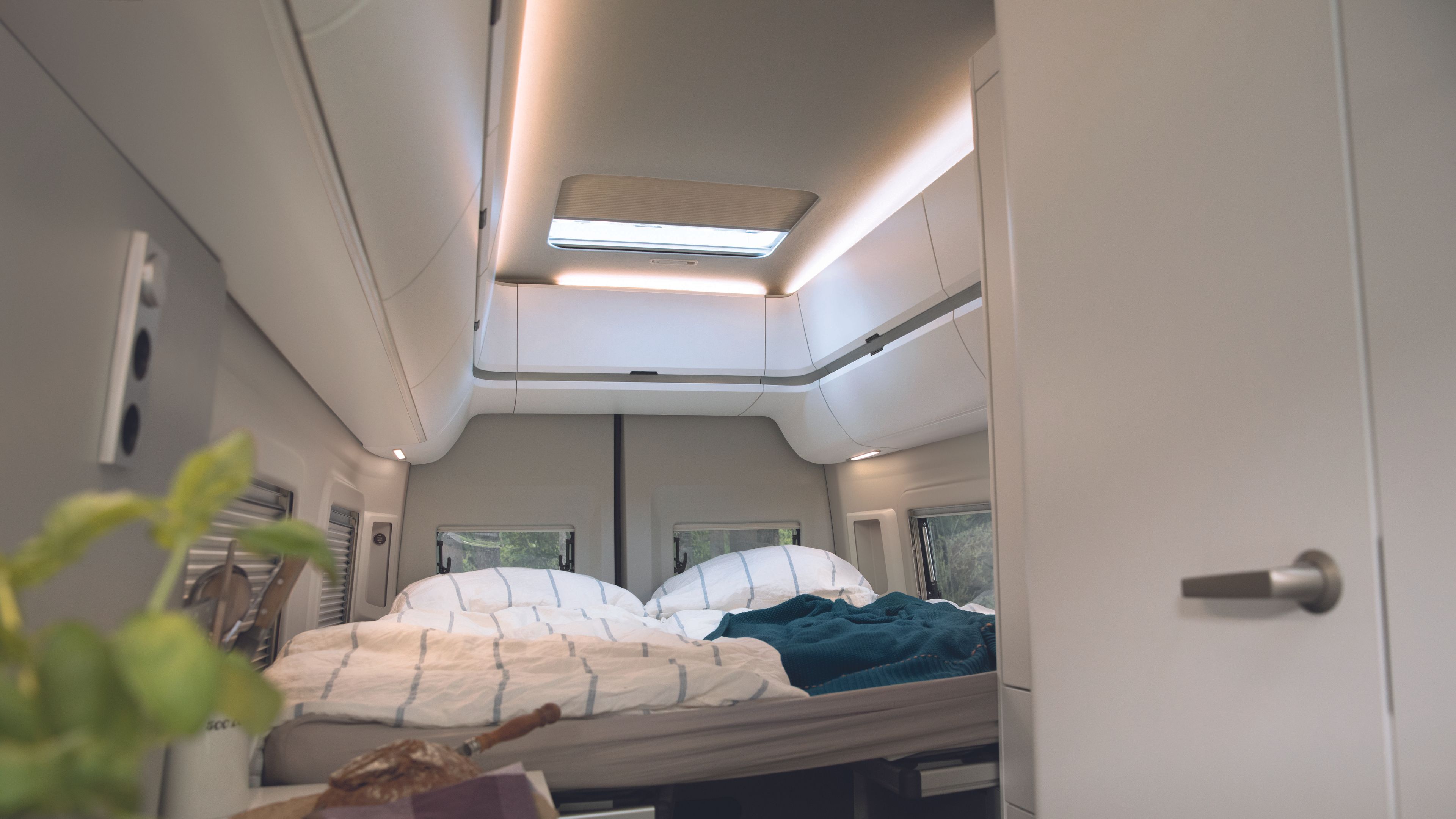 A fotografia mostra a cama na Grand California 680 com iluminação interior acolhedora. 