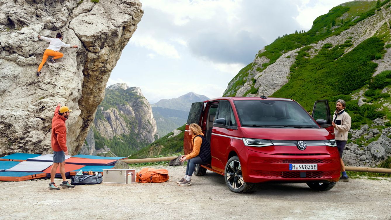 Volkswagen Multivan numa paisagem de montanhas com um grupo de pessoas a escalar.