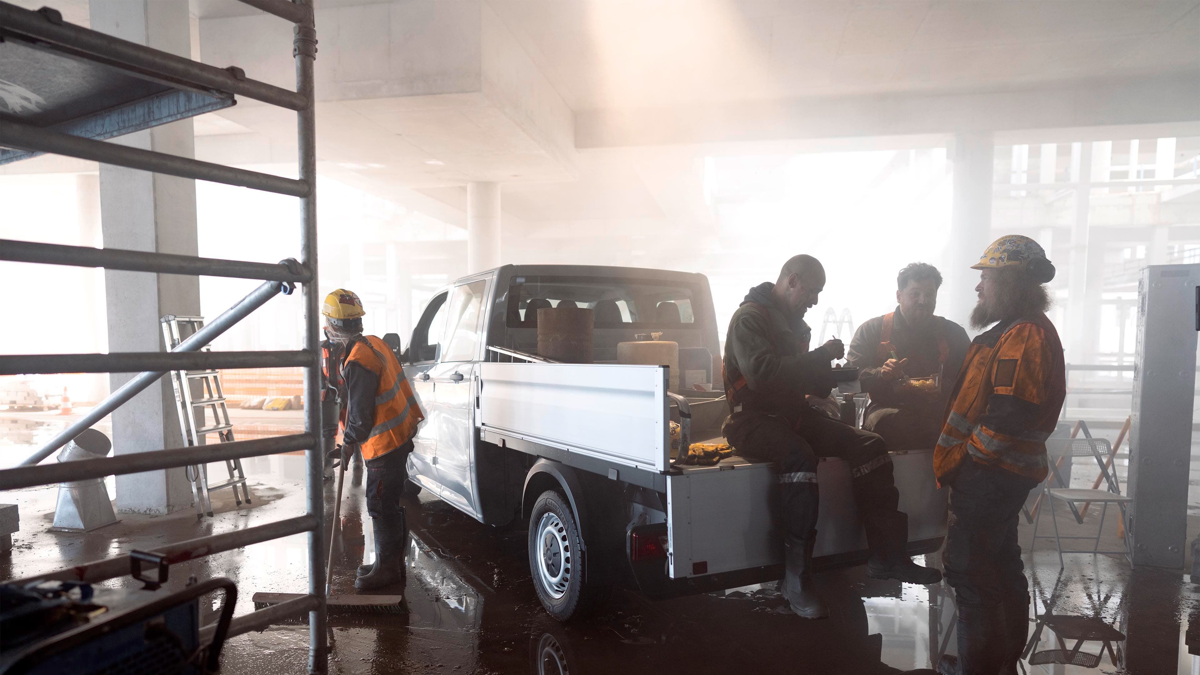 Vários trabalhadores da construção civil a fazer uma pausa à volta de um Volkswagen Crafter com plataforma de carga.