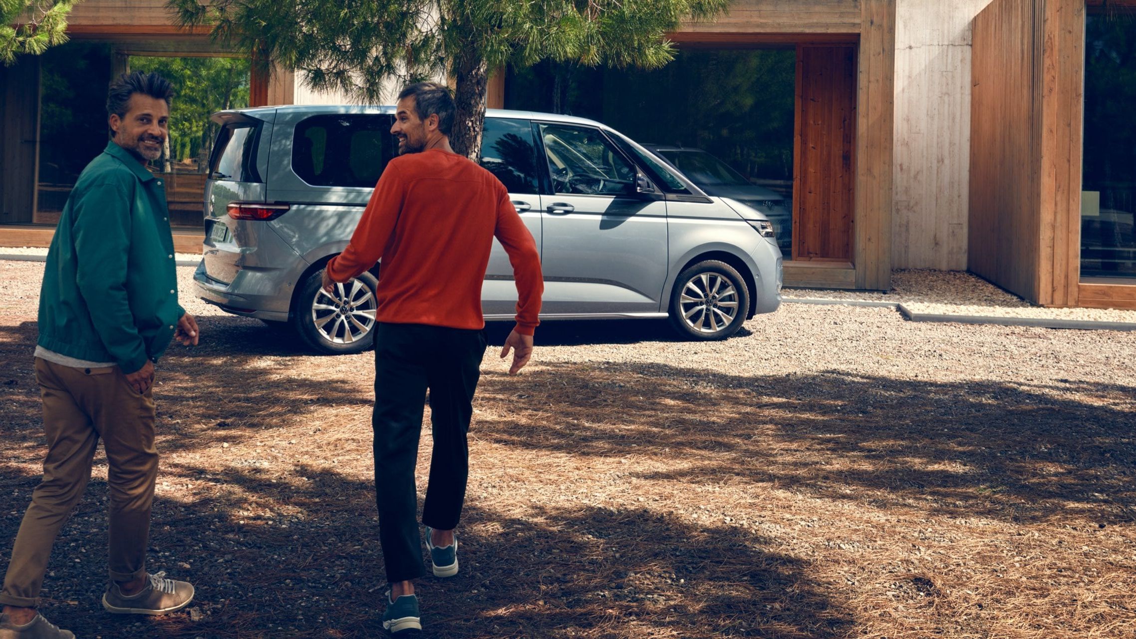 Dois homens correm para uma VW Multivan Life estacionado.
