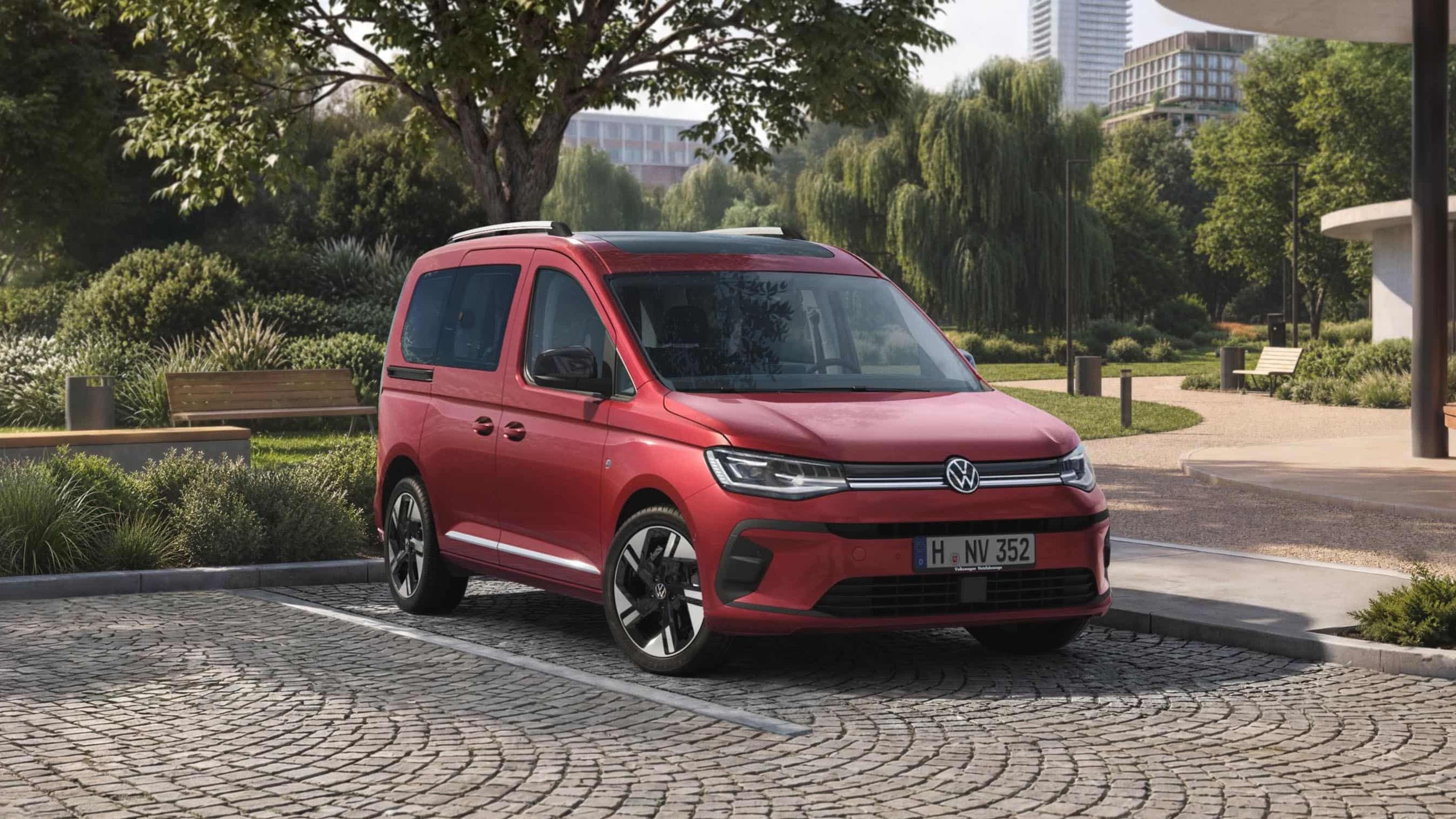 VW Caddy vermelha num estacionamento em frente a um parque numa cidade.