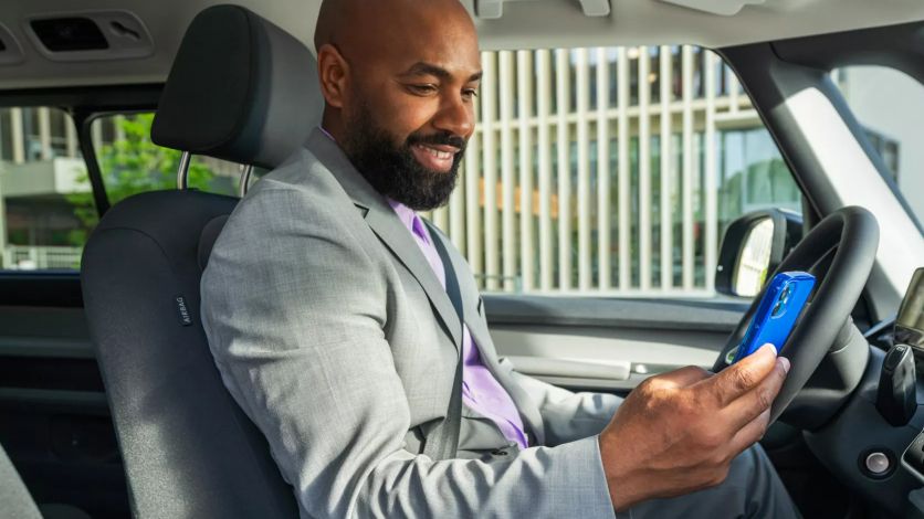 Um homem olha para o seu smartphone sentado ao volante do seu VW ID. Buzz estacionado.
