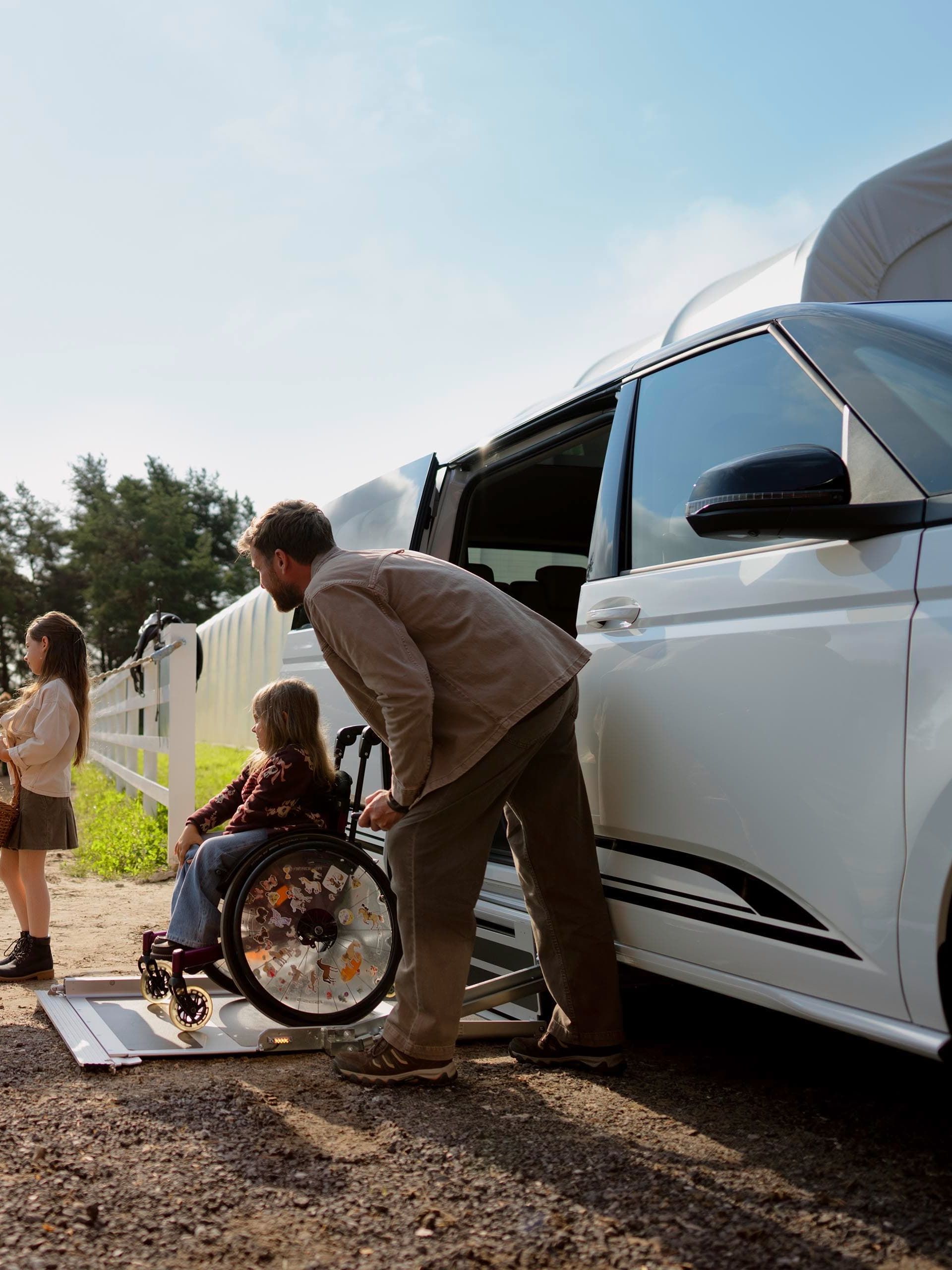 Uma criança em cadeira de rodas sai de um Volkswagen Caddy com rampa para cadeiras de rodas. 
