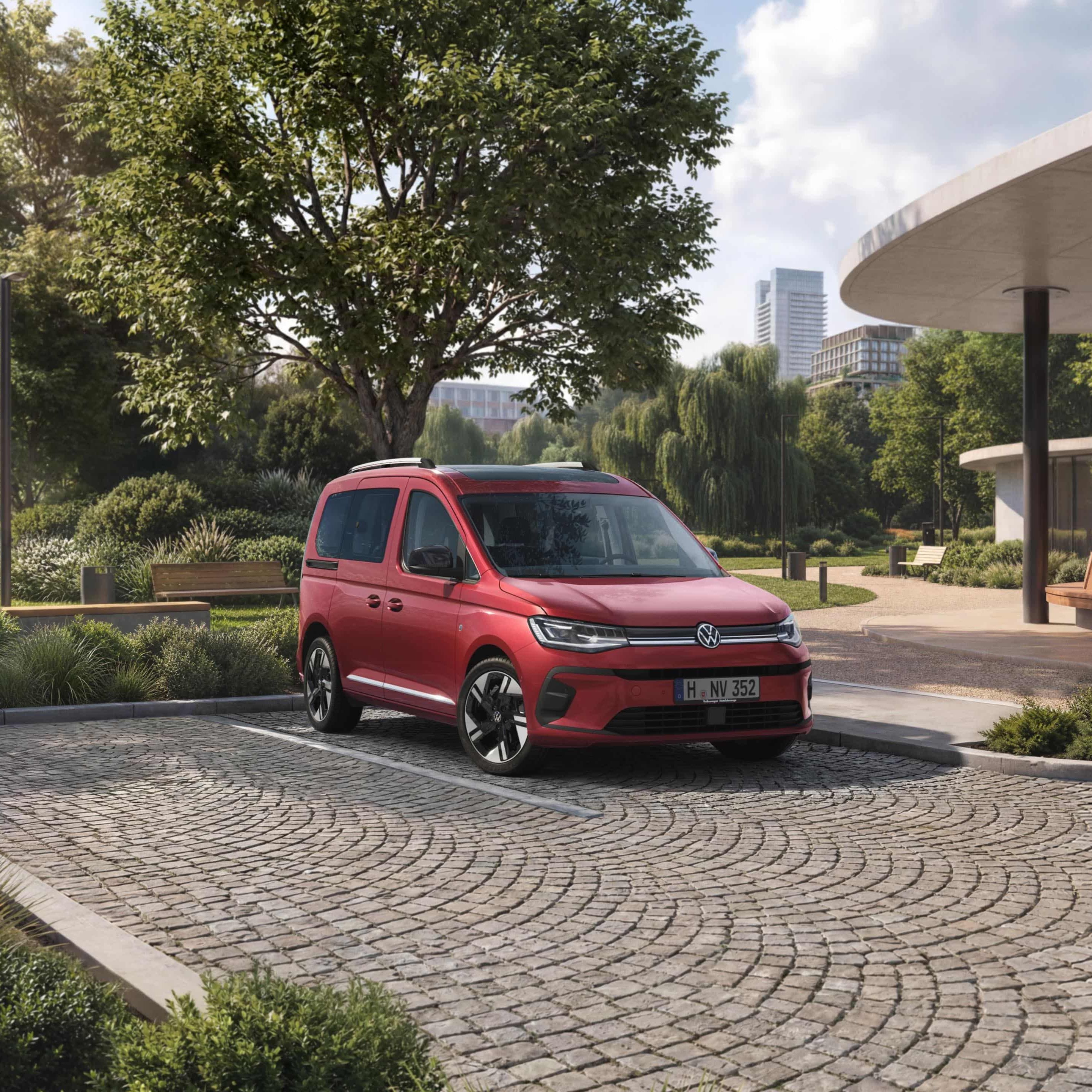 VW Caddy vermelha num estacionamento em frente a um parque numa cidade.