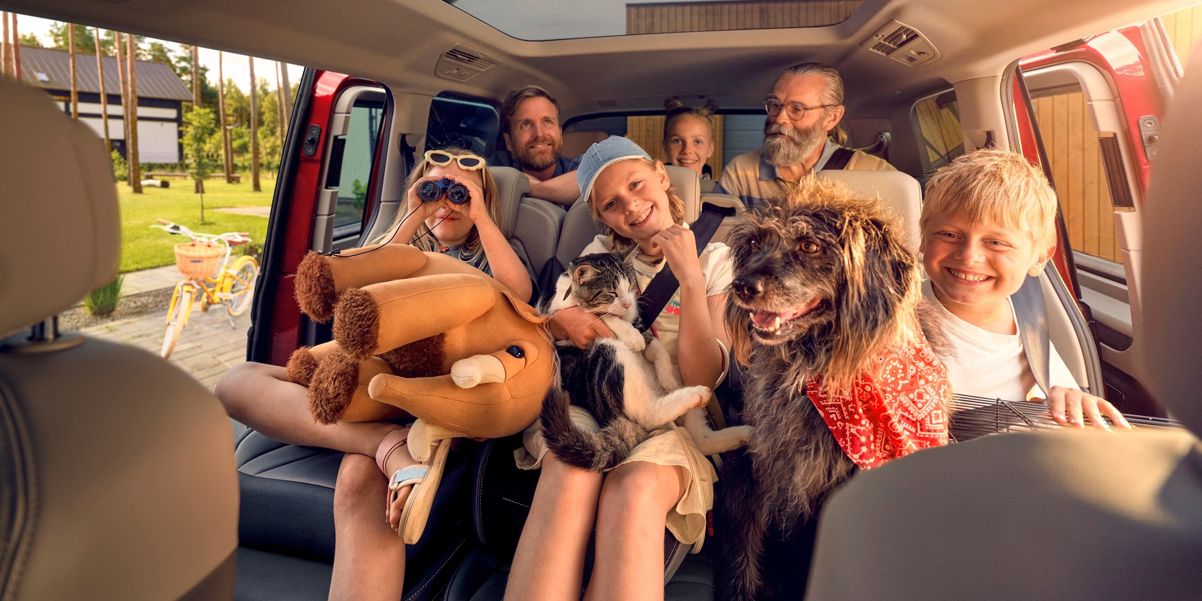Uma família numerosa com um cão, um gato e um peluche nas duas filas de bancos traseiras de uma Volkswagen Multivan.