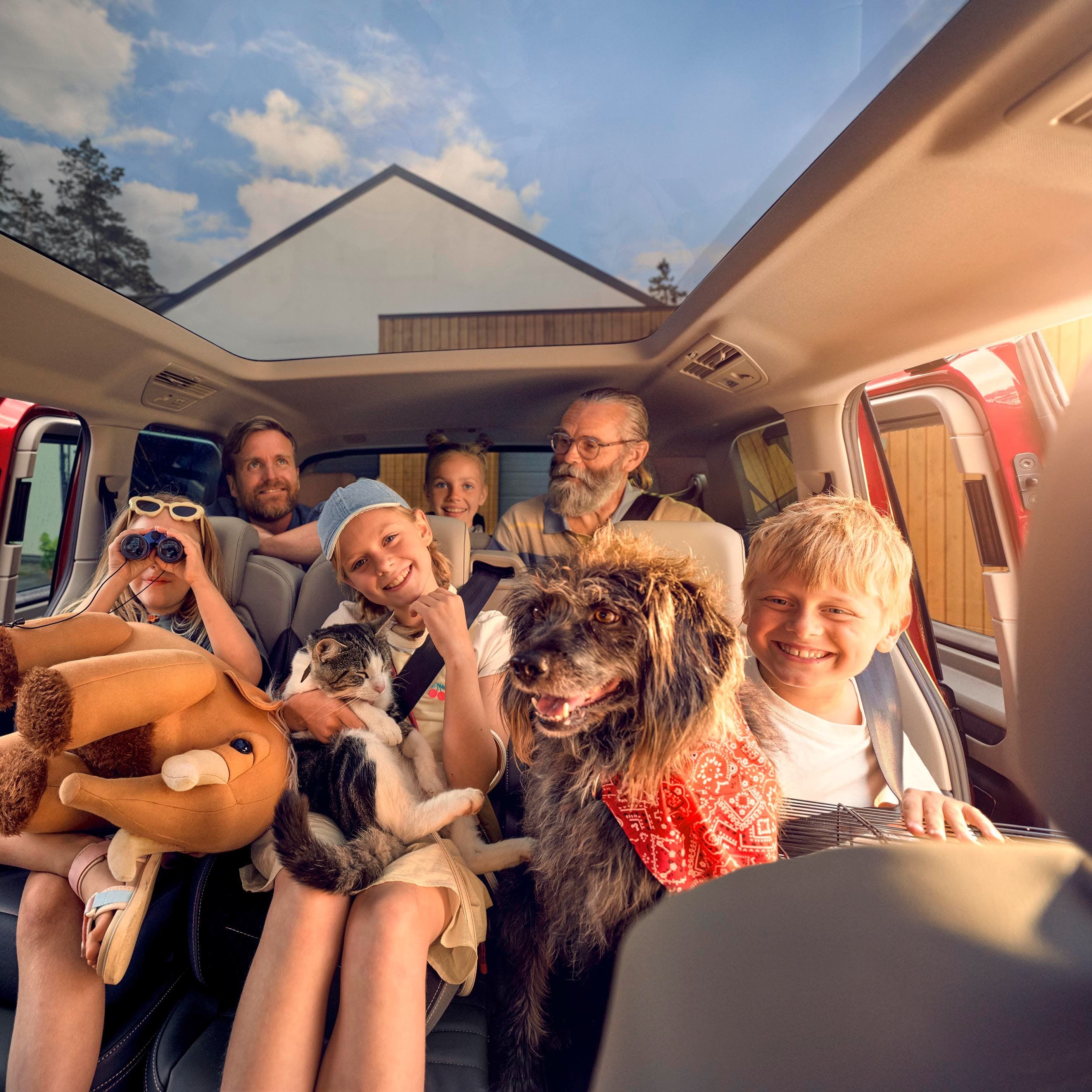 Uma família numerosa com um cão, um gato e um peluche nas duas filas de bancos traseiras de uma Volkswagen Multivan.