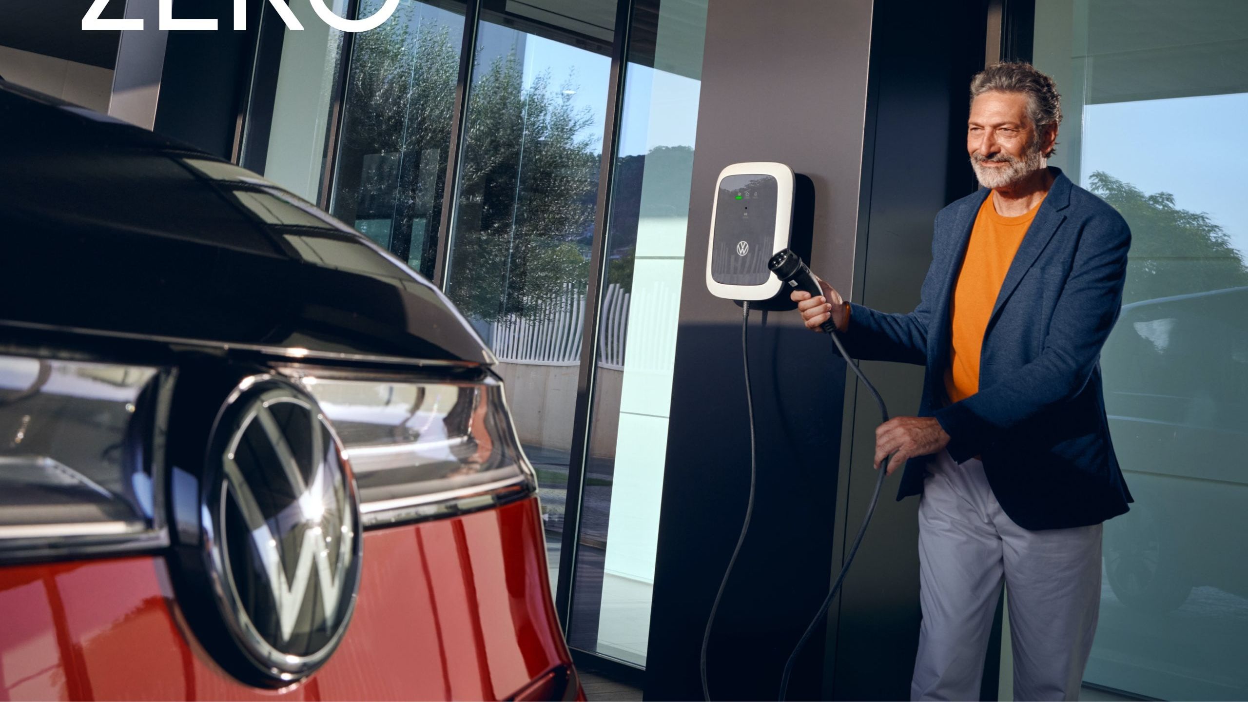 Um homem segura um cabo de carregamento. Pode ver-se a VW Multivan Style.