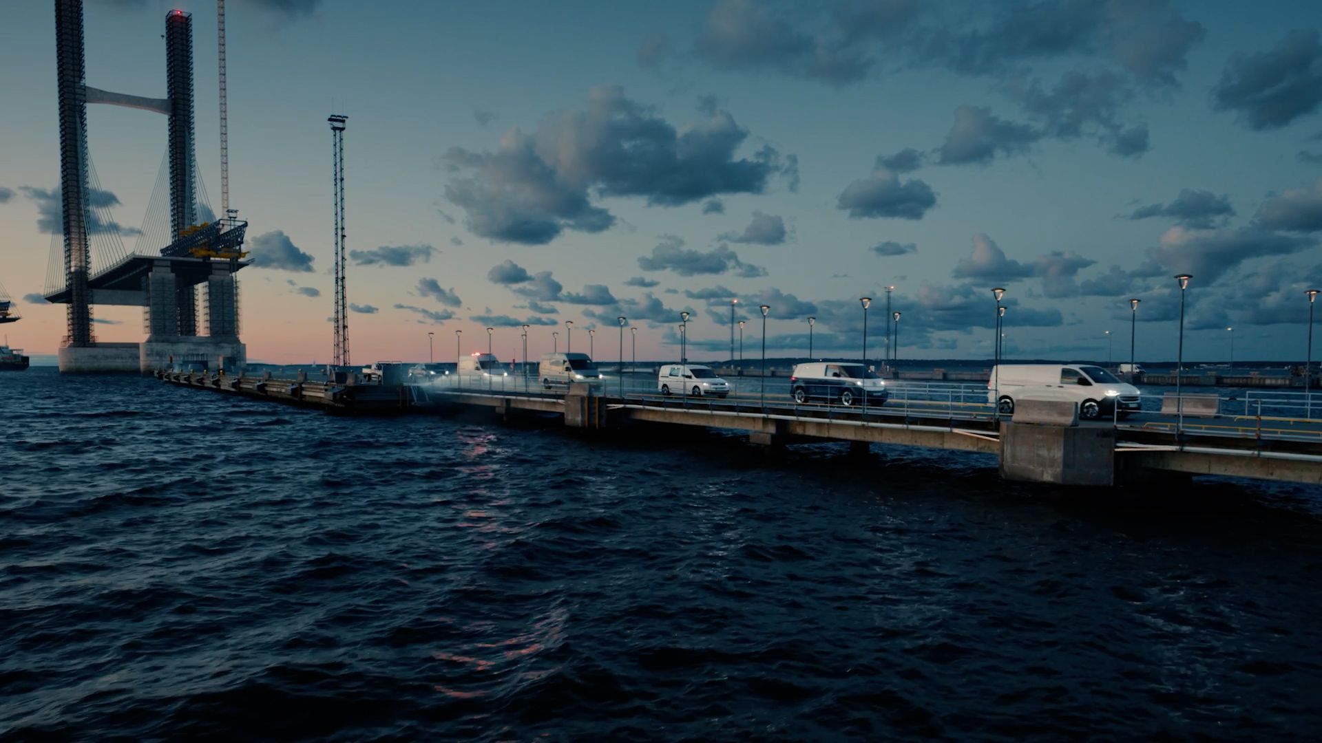 Uma série de veículos comerciais Volkswagen a caminho de casa, vindos de um estaleiro de construção numa ponte.