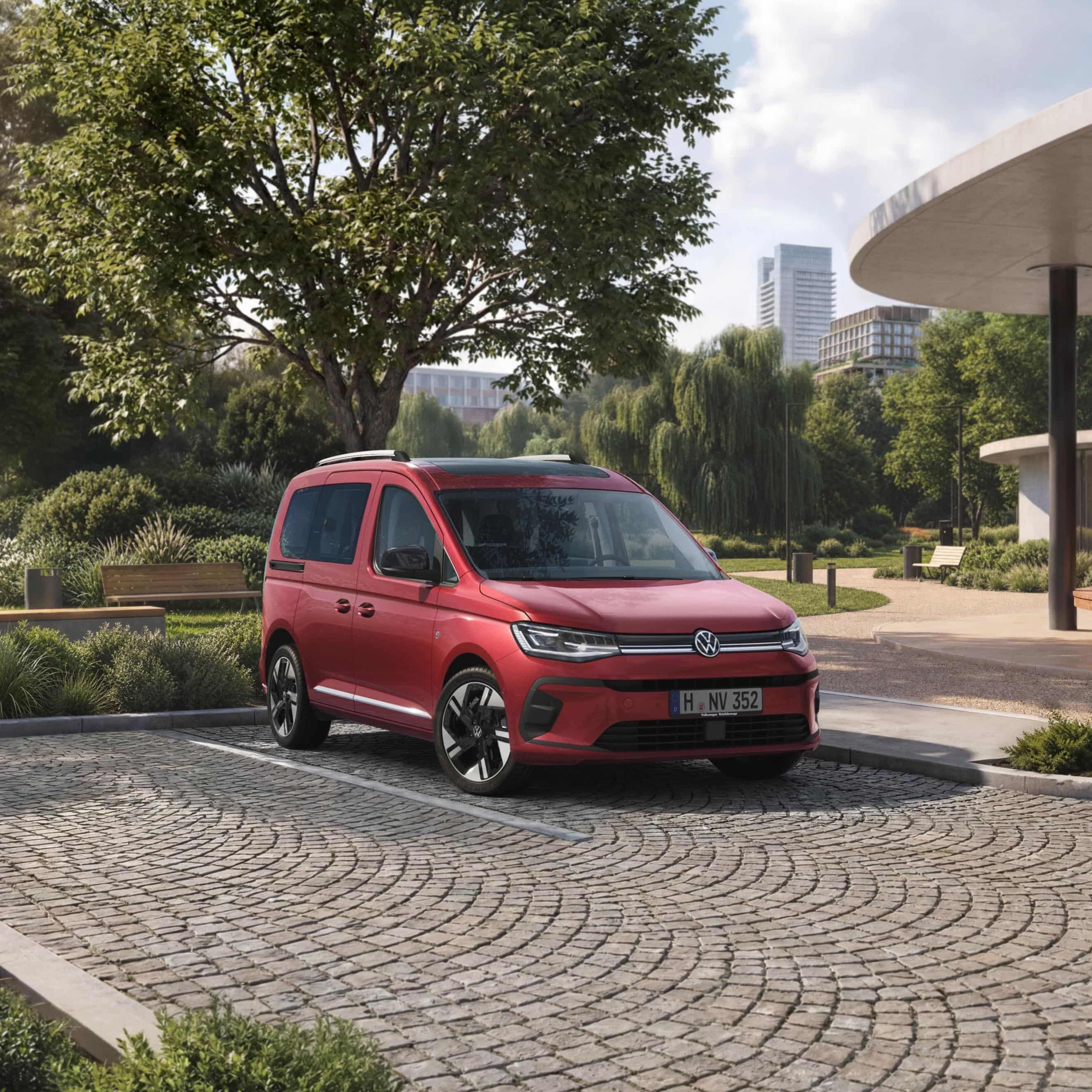 VW Caddy vermelha num estacionamento em frente a um parque numa cidade.
