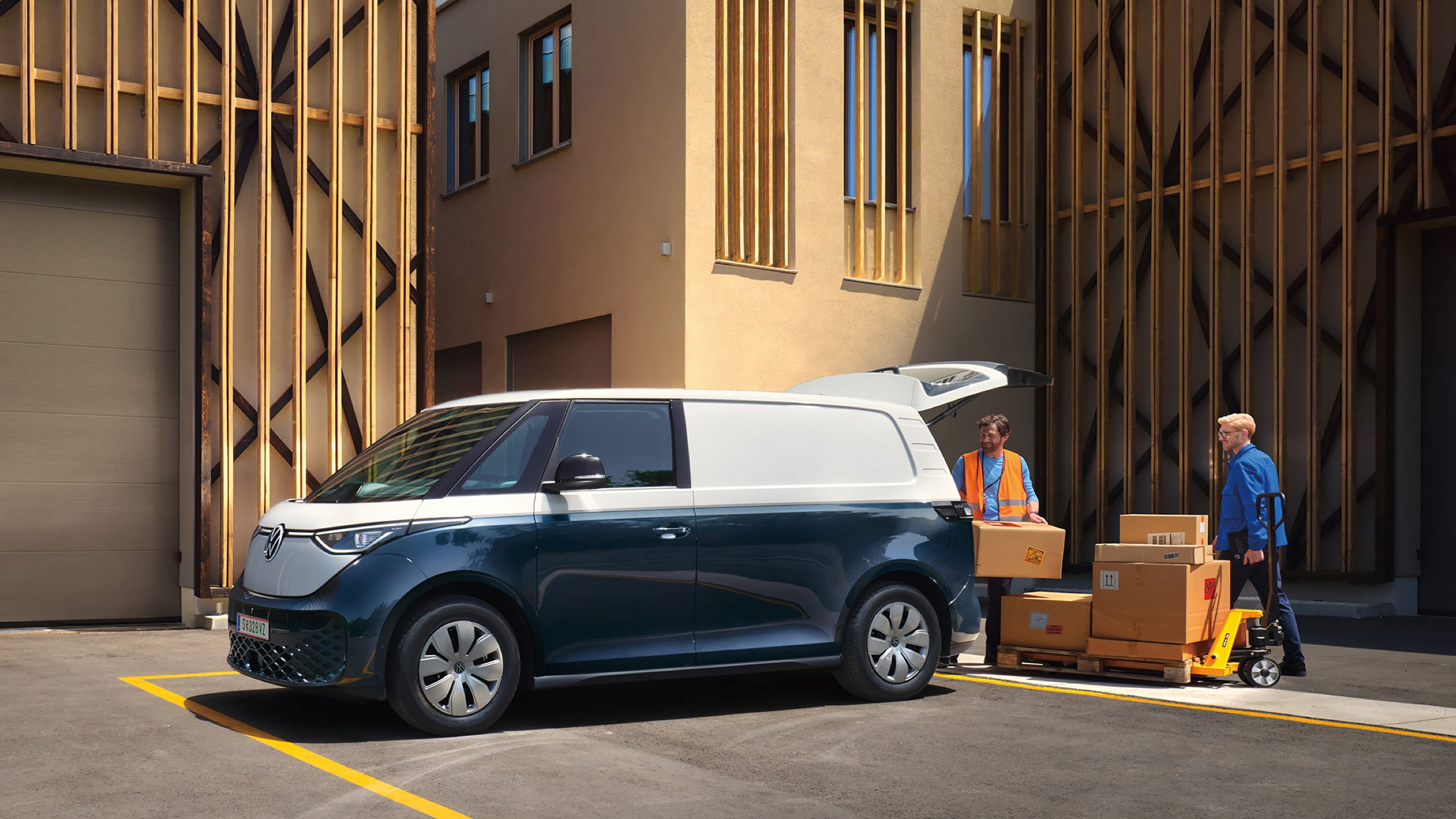 Zwei Personen beladen einen weiß blauen ID. Buzz Cargomit Kartons durch das Heck