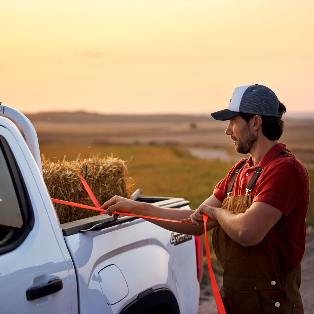 Ein Mann zurrt einen Strohballen an der Ladefläche eines Volkswagen Amarok fest.