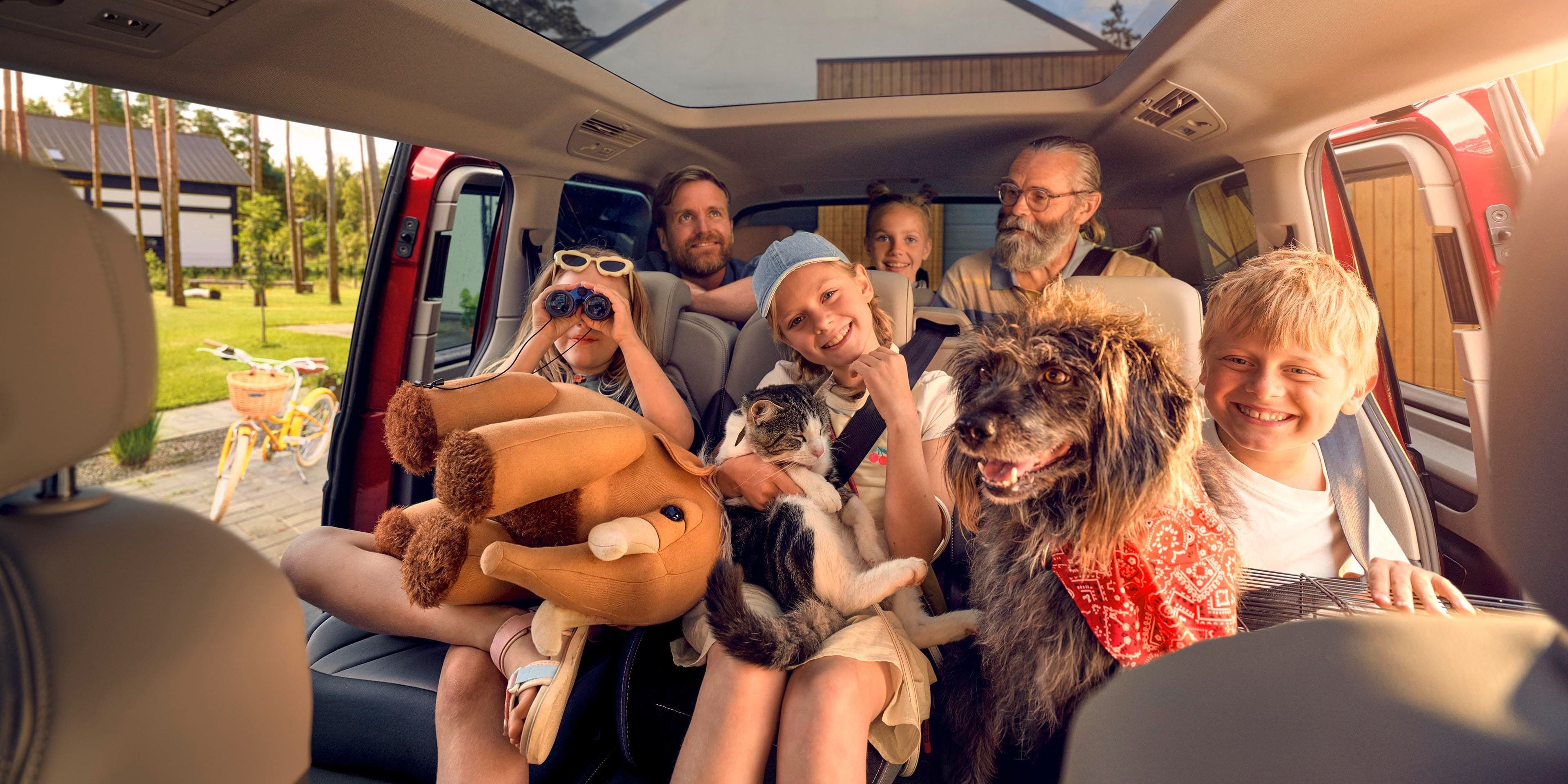 Uma família numerosa com um cão, um gato e um peluche nas duas filas de bancos traseiras de uma Volkswagen Multivan.