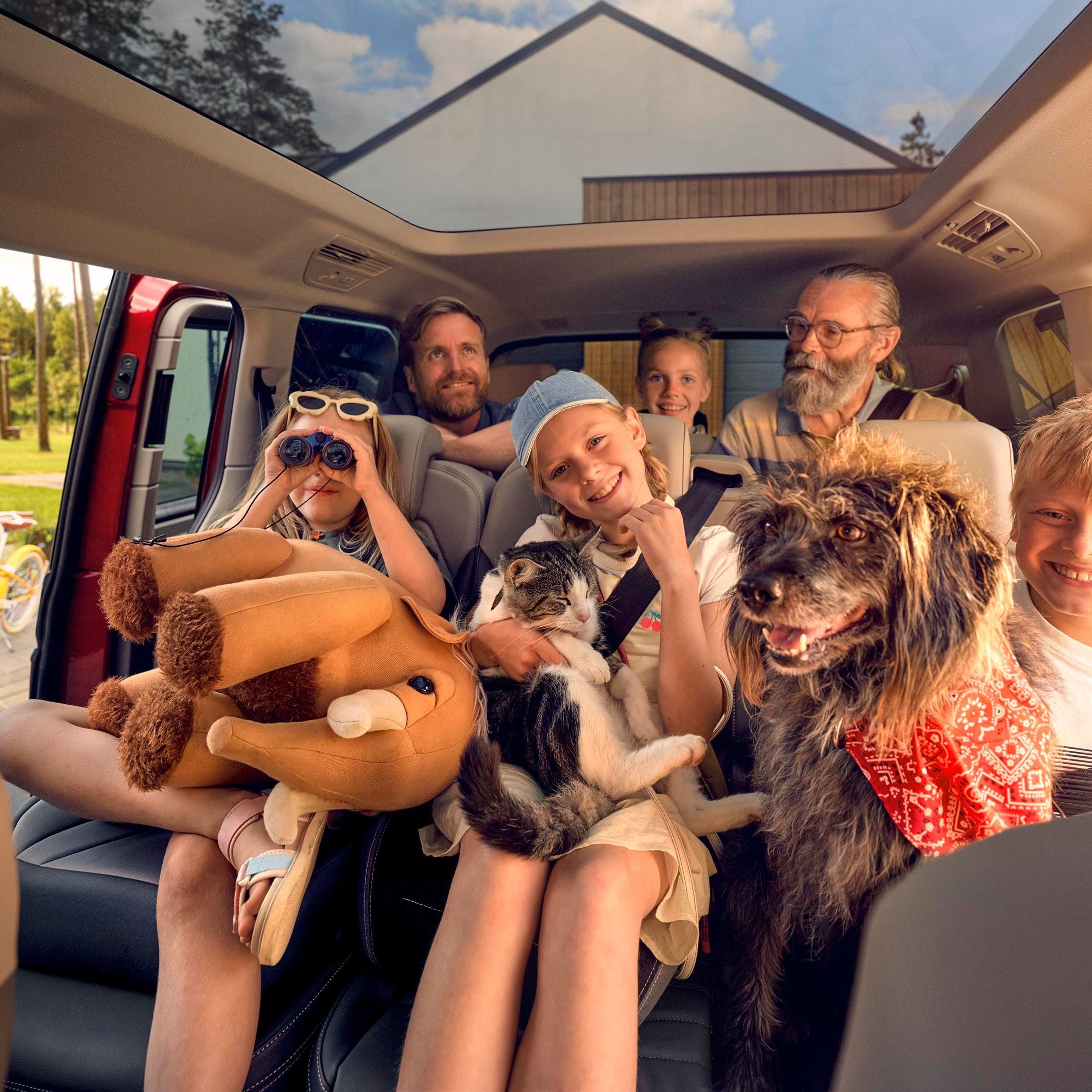 Uma família numerosa com um cão, um gato e um peluche nas duas filas de bancos traseiras de uma Volkswagen Multivan.