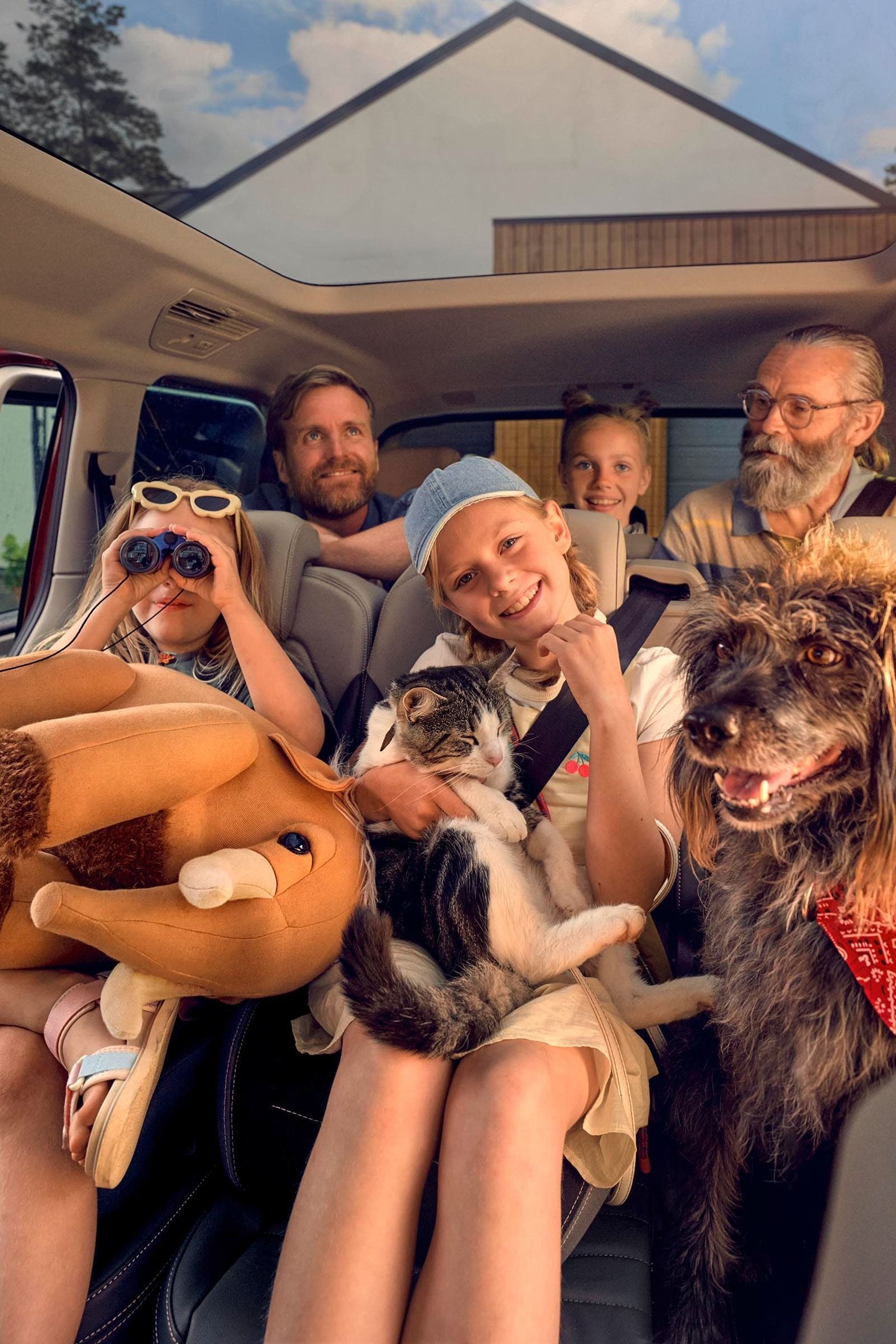 Uma família numerosa com um cão, um gato e um peluche nas duas filas de bancos traseiras de uma Volkswagen Multivan.