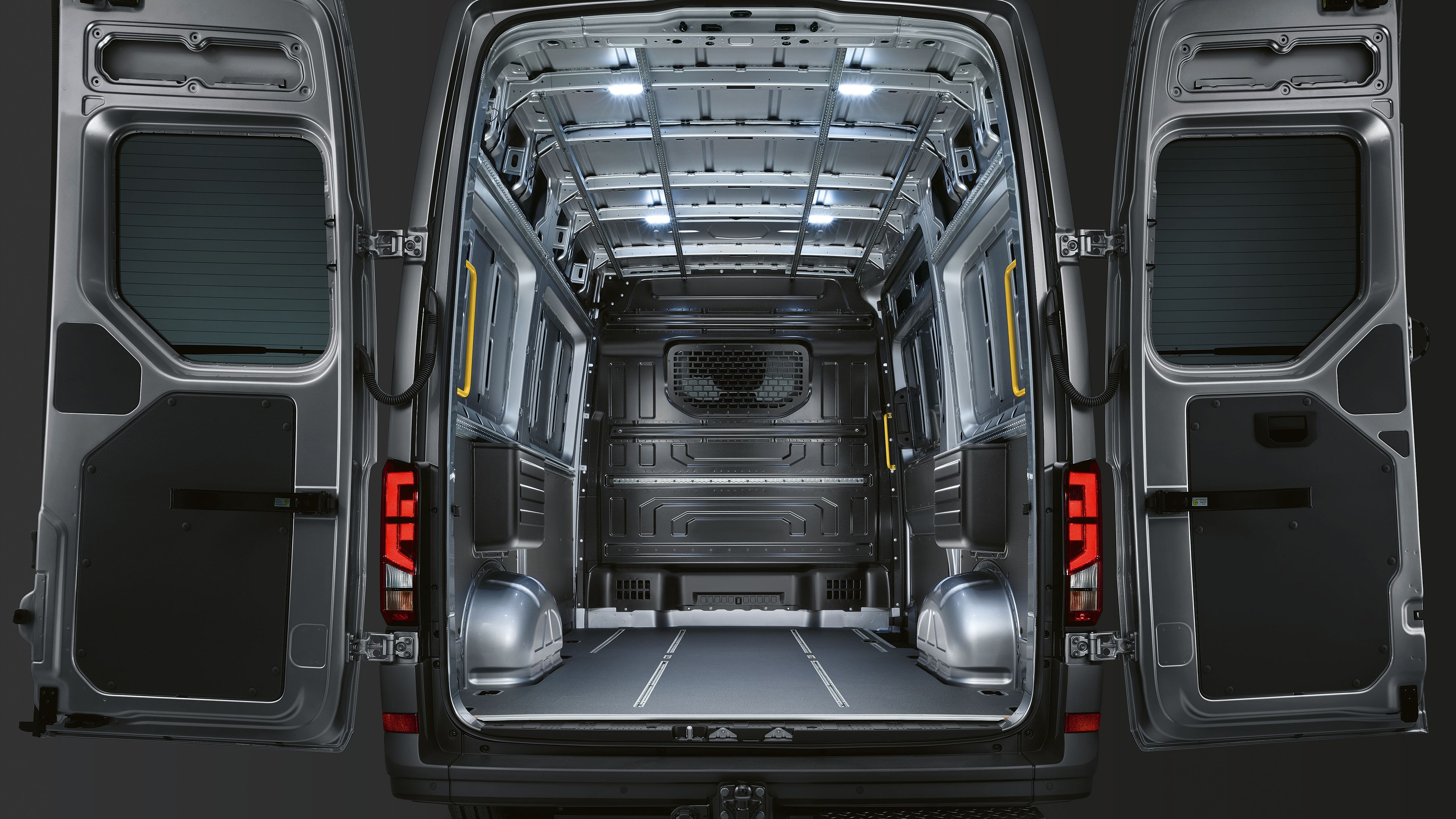 O VW Crafter Cargo parado num espaço escuro. As suas portas traseiras de abertura lateral abertas até trás deixam ver o compartimento de carga vazio.O compartimento da carrinha é iluminado pelos quatro LED montados sob o tejadilho.