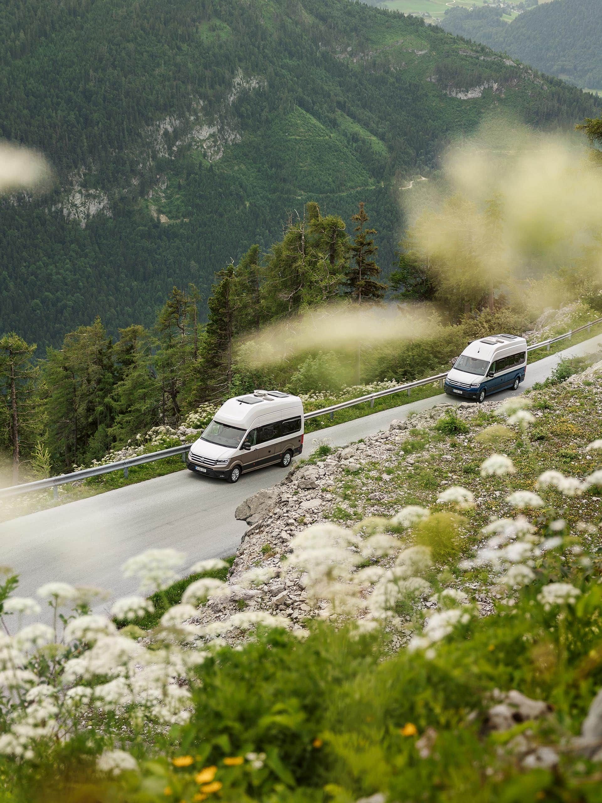 Duas Grand California a passar por um desfiladeiro de montanha verde.