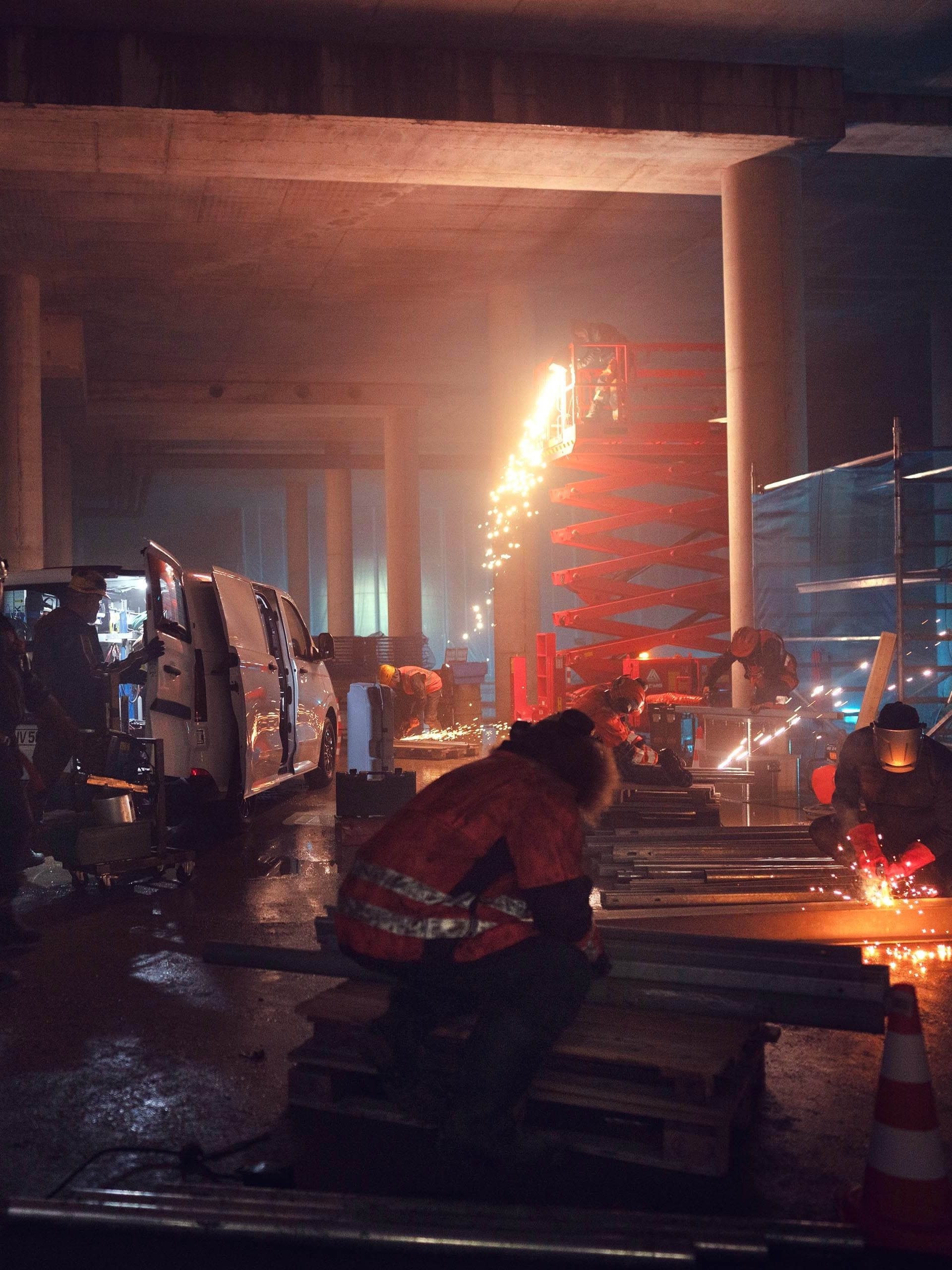 Trabalhadores da construção civil cortam metal, faúlhas iluminam a cena.