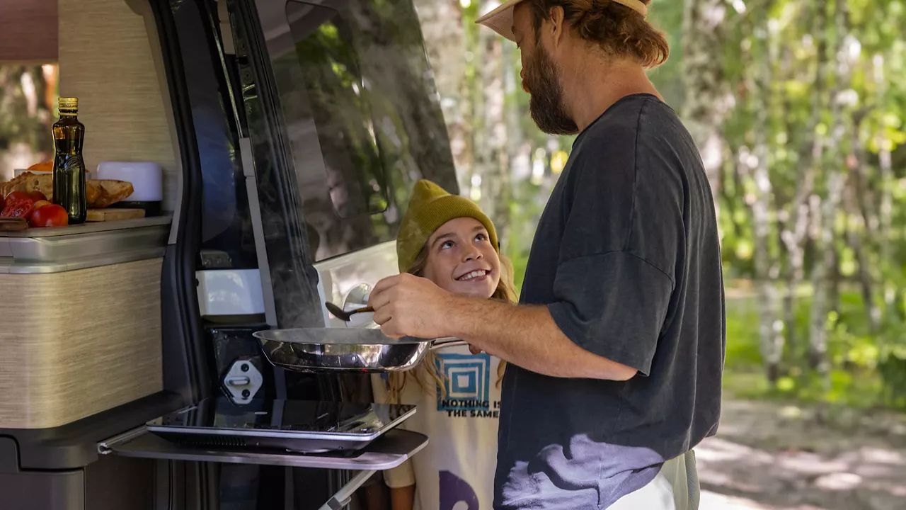 Um pai cozinha no fogão da Volkswagen California.