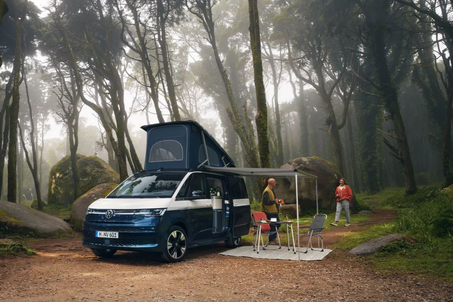 Um casal estacionado com a sua Volkswagen California junto a um lago admira a natureza.