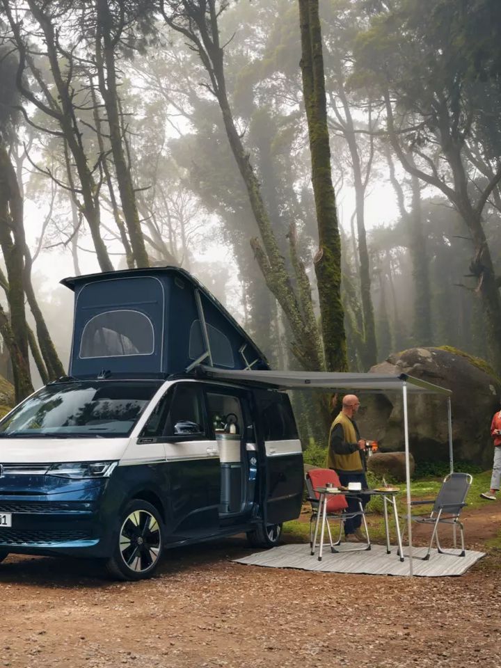 Um casal estacionado com a sua Volkswagen California junto a um lago admira a natureza.