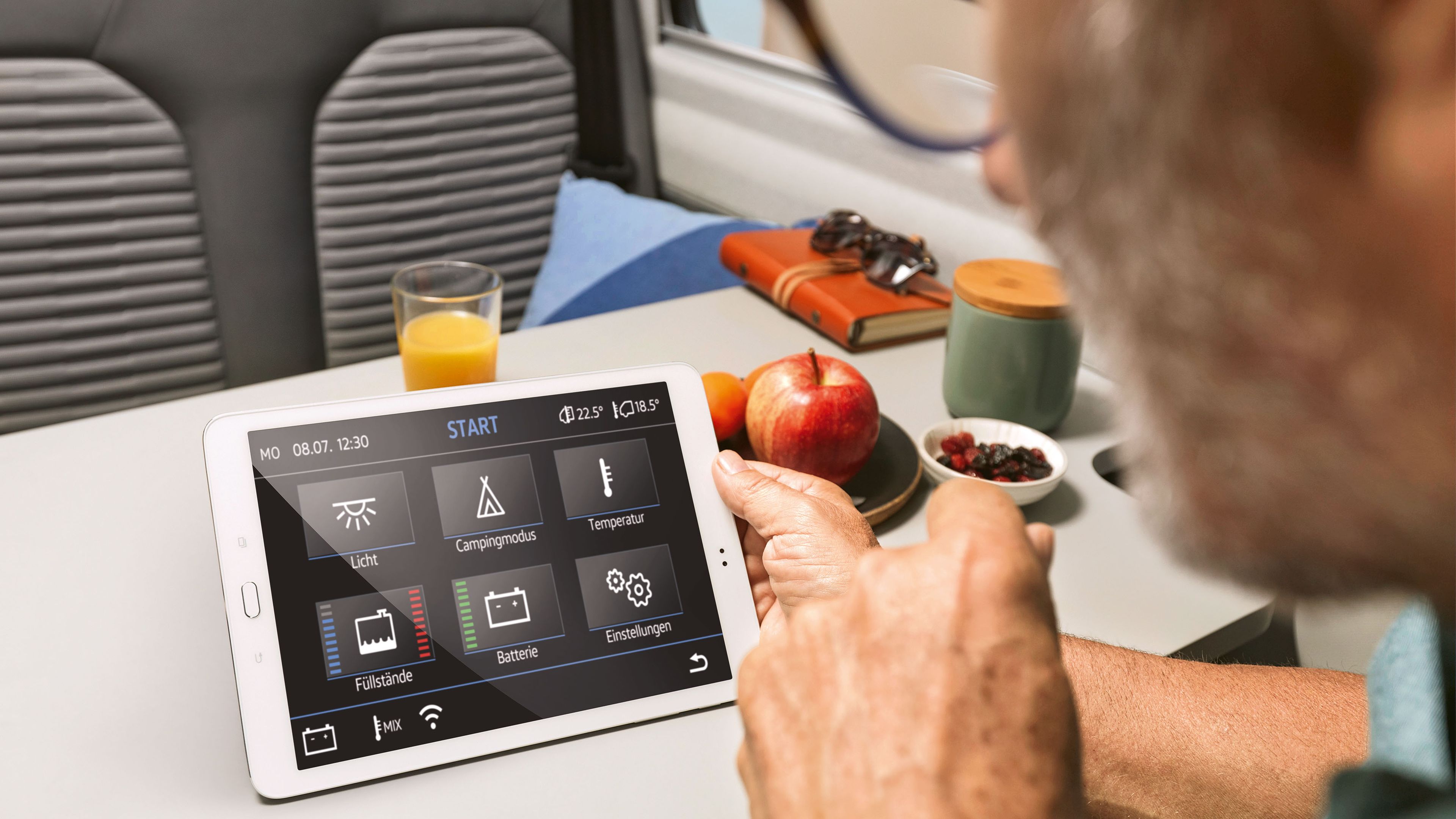 O homem clica no seu tablet. Mostra opções importantes de veículos, tais como a temperatura, os níveis do depósito de água e o estado de carga da bateria. 