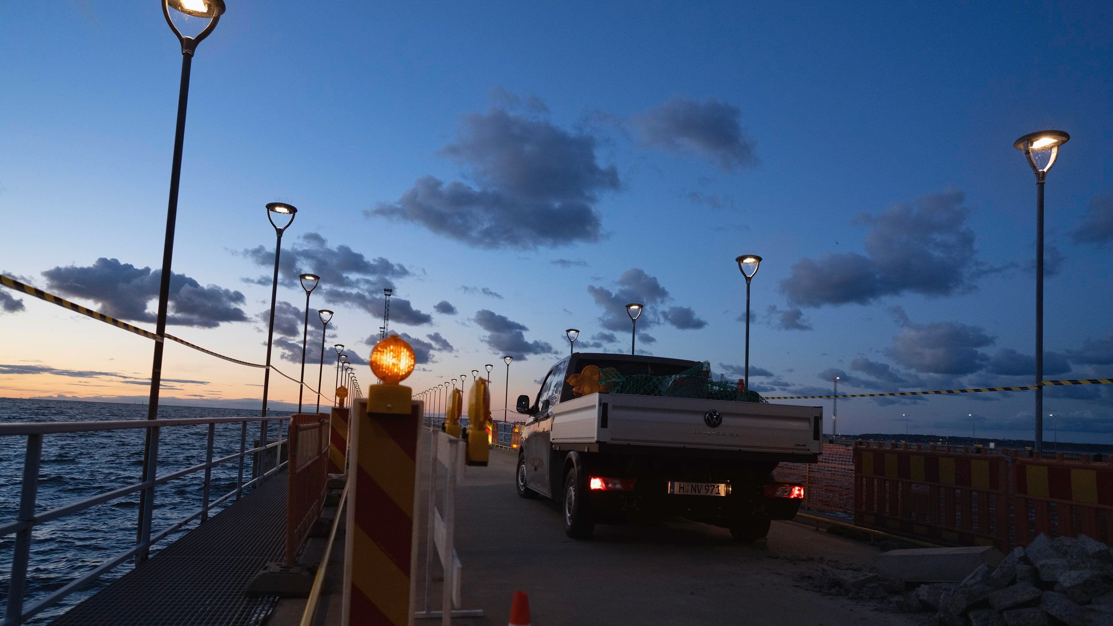 Um Volkswagen Crafter com plataforma de carga estacionada num estaleiro junto à água.