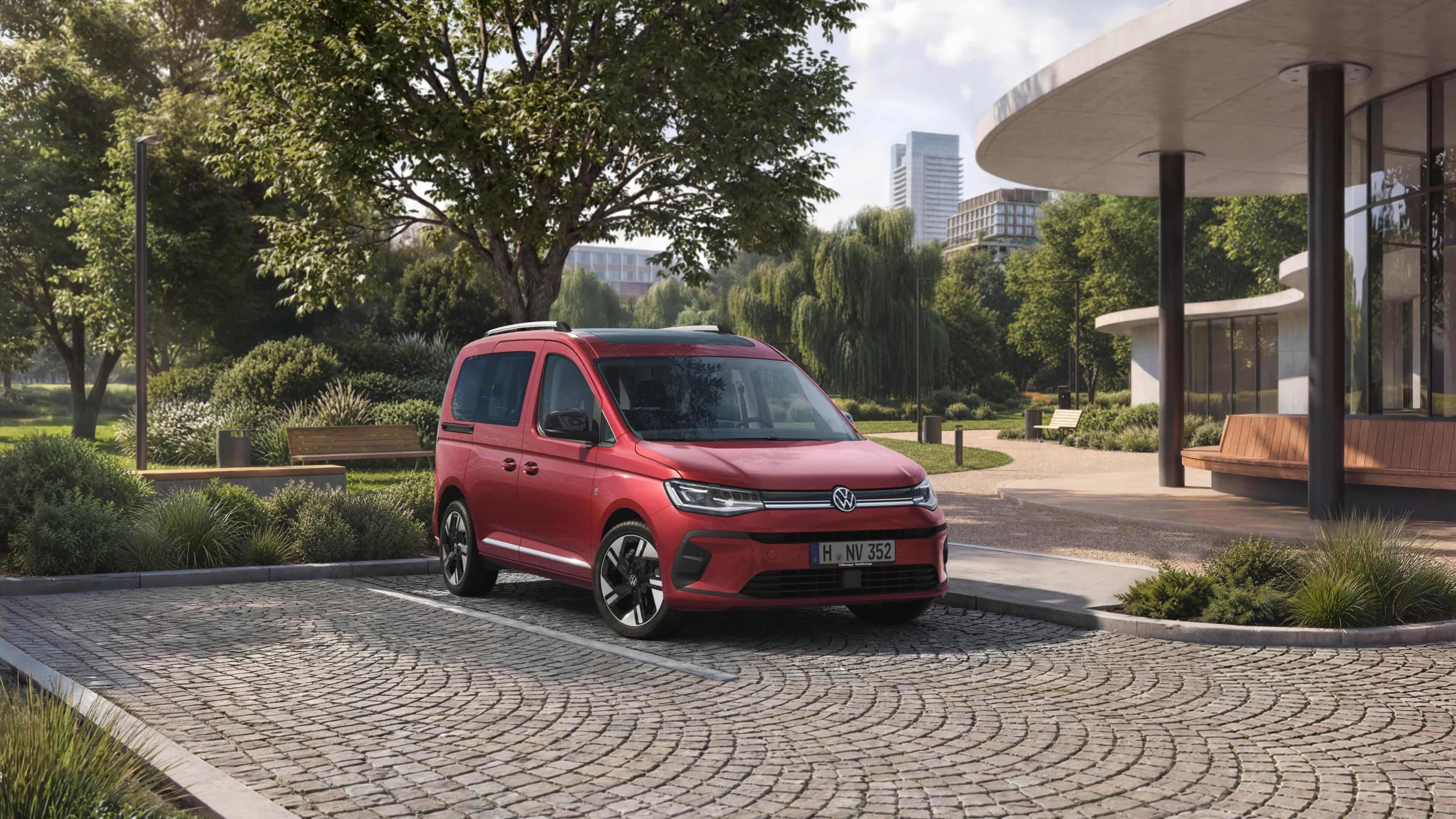 VW Caddy vermelha num estacionamento em frente a um parque numa cidade.