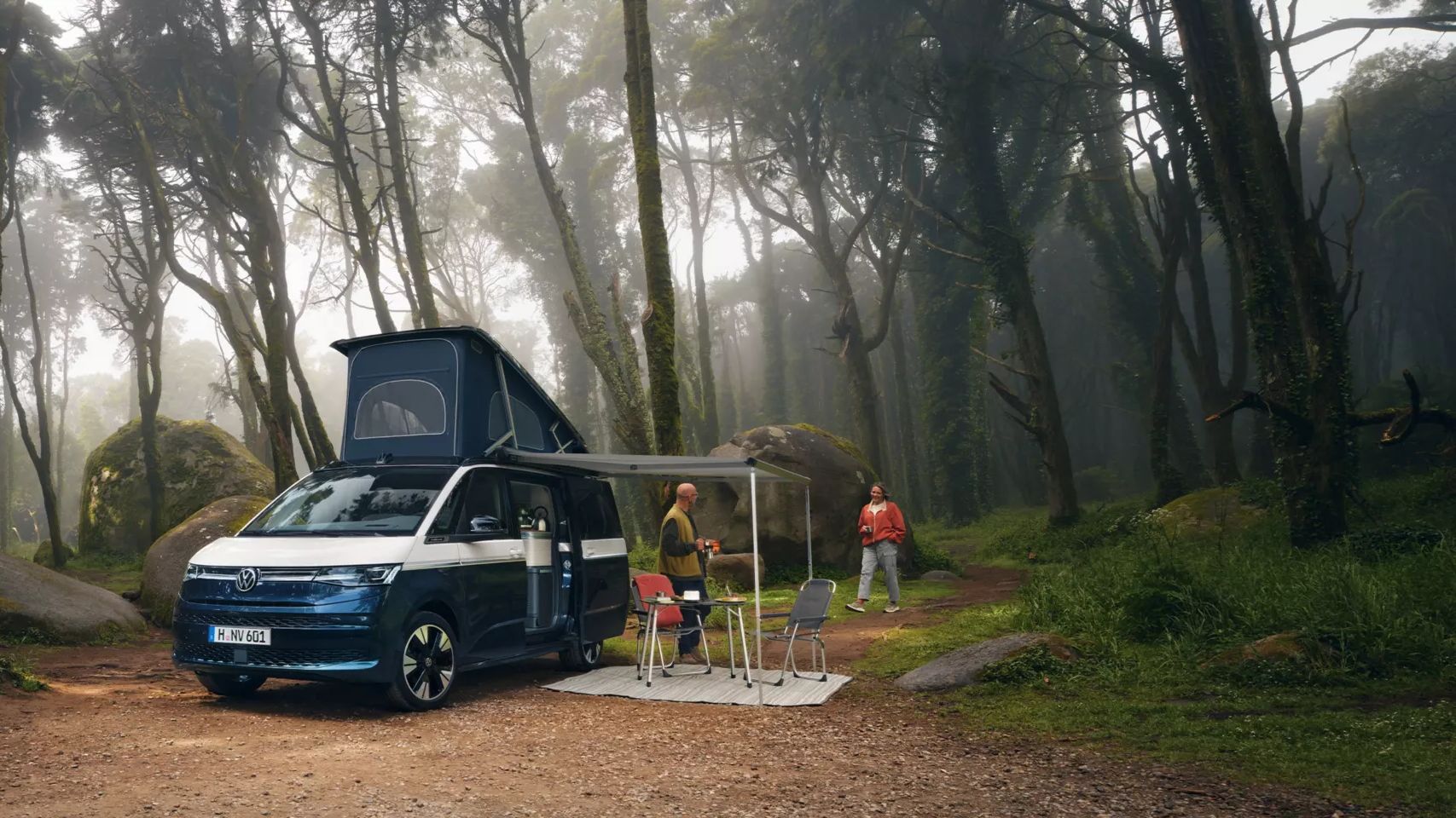 Um casal estacionado com a sua Volkswagen California junto a um lago admira a natureza.
