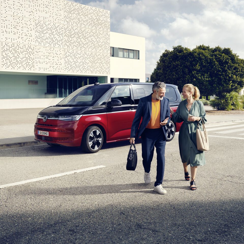 Ein Paar läuft vor einem neuen VW Multivan T7 2021 Style. 