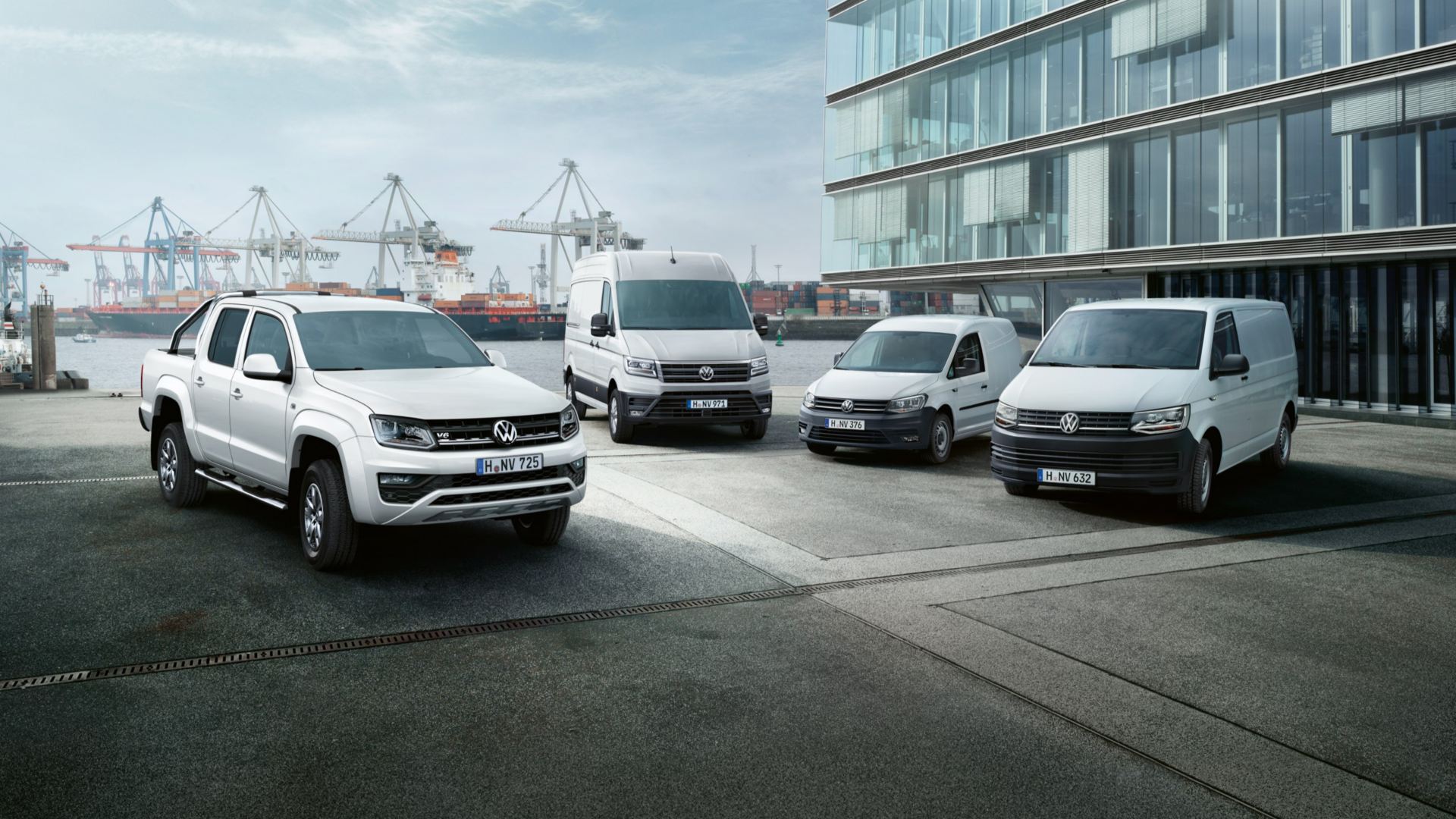 Uma gama de veículos comerciais Volkswagen estacionados à frente de um cenário portuário