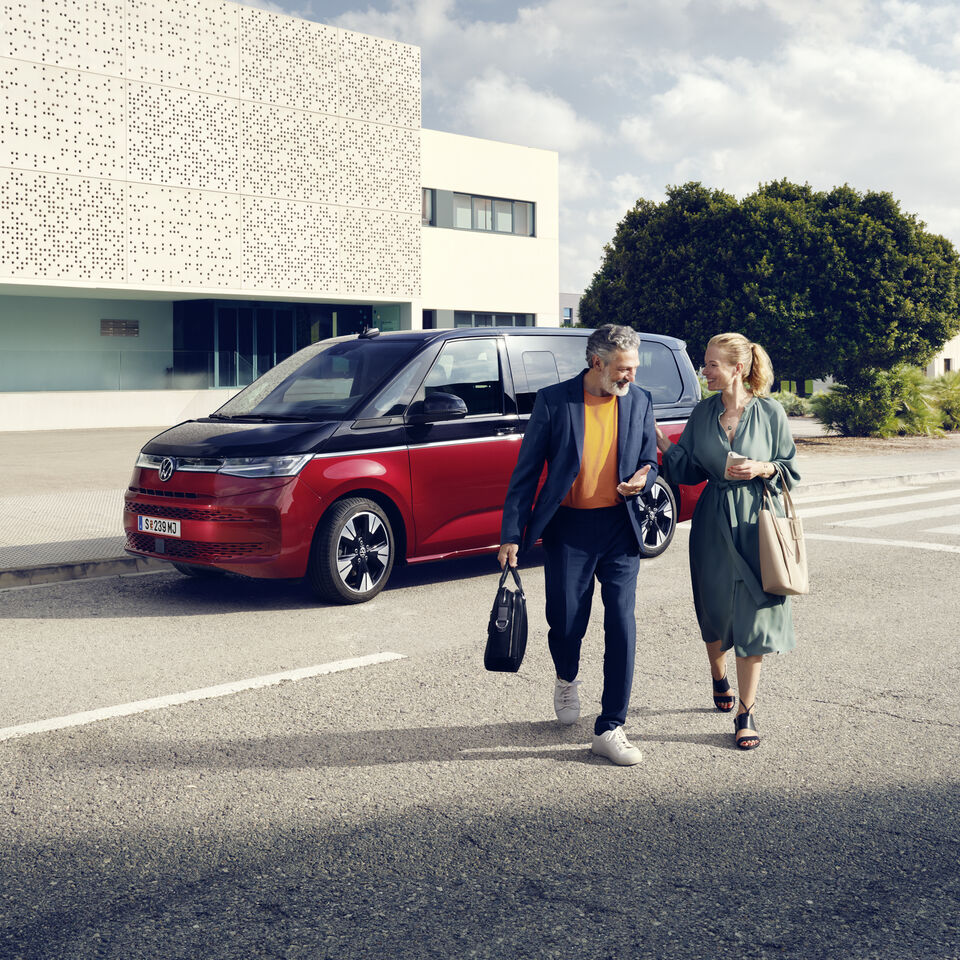 Ein Paar läuft vor einem neuen VW Multivan T7 2021 Style. 