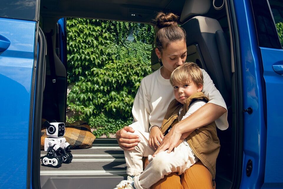 Eine Mutter sitzt mit ihrem Sohn im Rahmen der Schiebetür des neuen VW Multivan T7 2021.