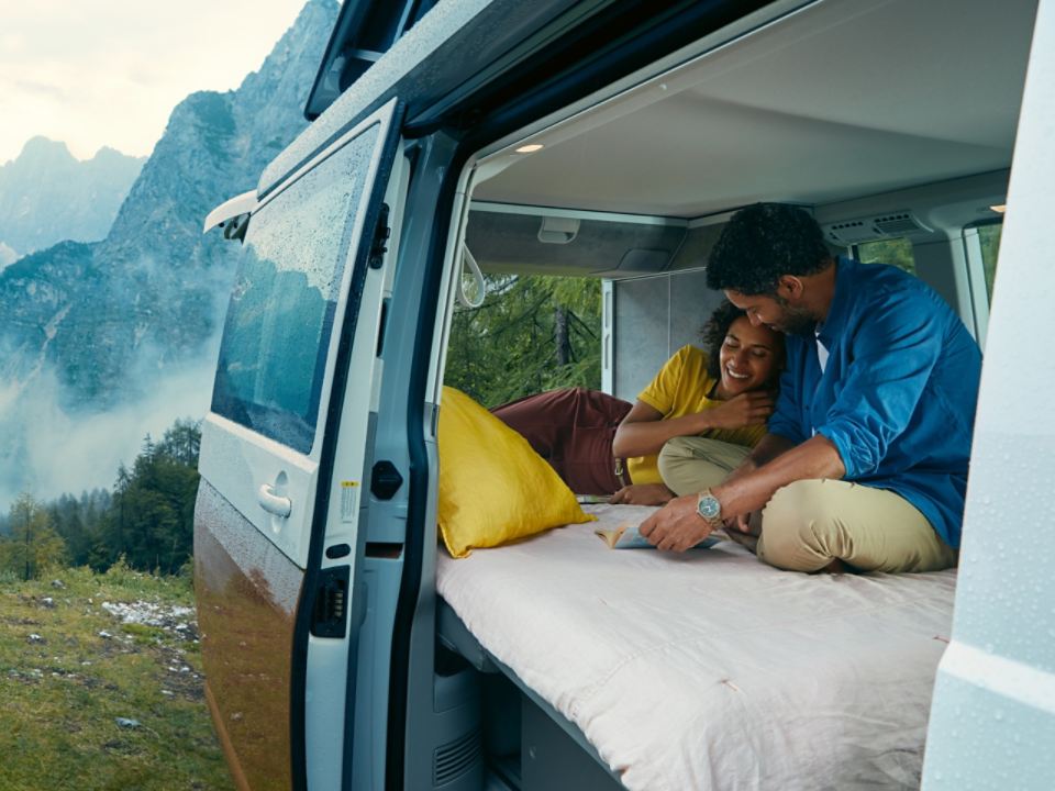 Um casal sentado na cama da autocaravana California 6.1, estacionada nas montanhas.