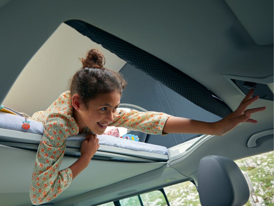 Uma rapariga a usar o painel de controlo da caravana da Volkswagen enquanto está deitada na cama alta da California 6.1.