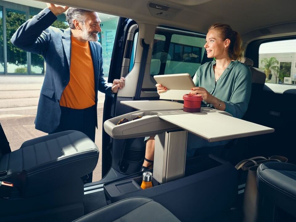 Eine Frau und ein Mann unterhalten sich am Multifunktionstisch im neuen VW Multivan T7 2021.