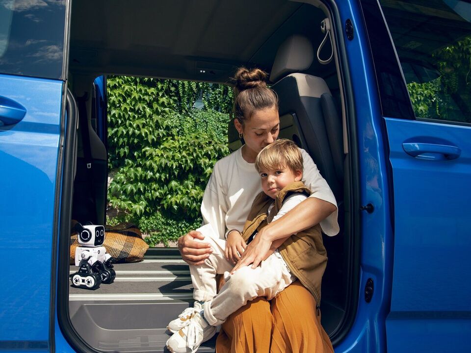 Eine Mutter sitzt mit ihrem Sohne im Rahmen der Schiebetür des VW Mutlivan T7 2021