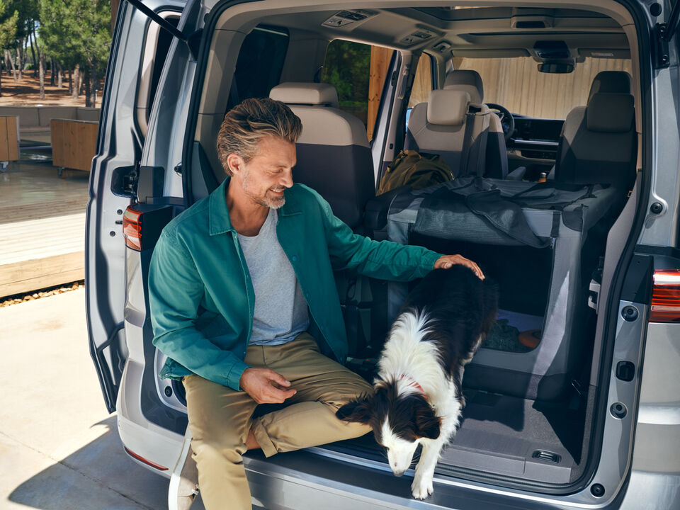 Um homem sentado na bagageira de uma VW Multivan Life com um cão.