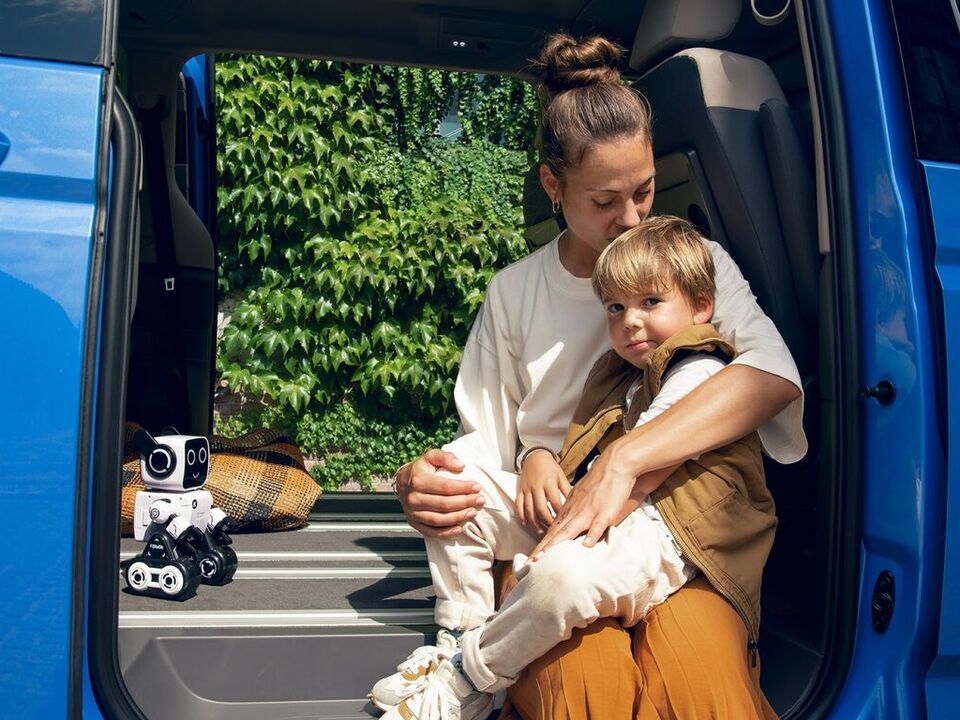 Uma mulher sentada com um rapaz na porta lateral do Multivan Energetic da Volkswagen.