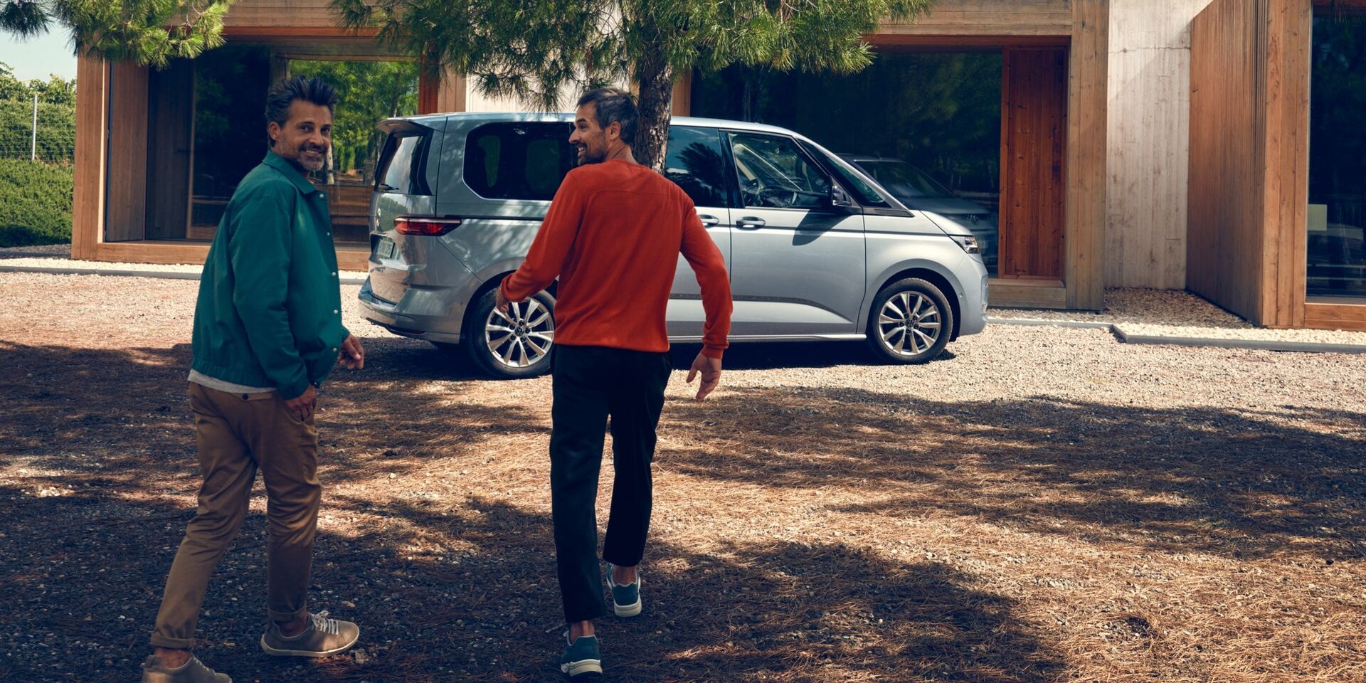 Dois homens correm para uma VW Multivan Life estacionado.