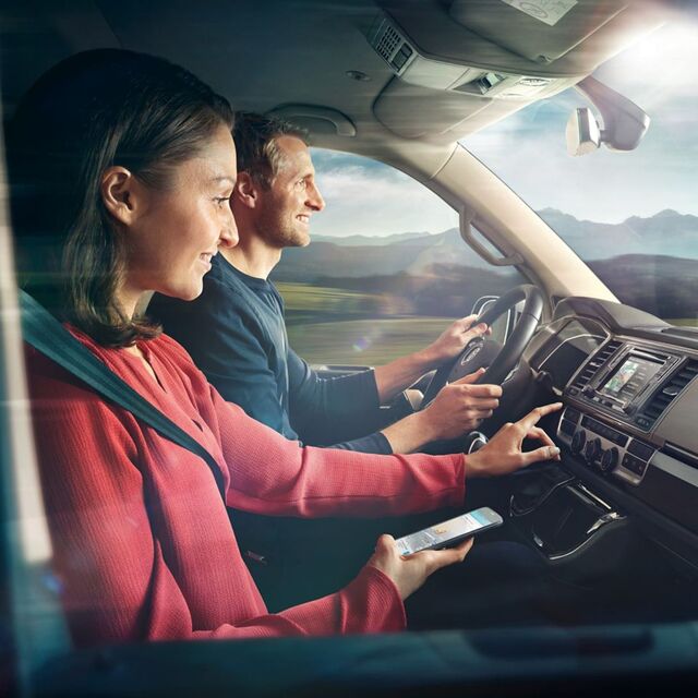 Eine Frau und ein Mann sitzen in einem VW Nutzfahrzeug, die Frau tippt gerade auf das Display