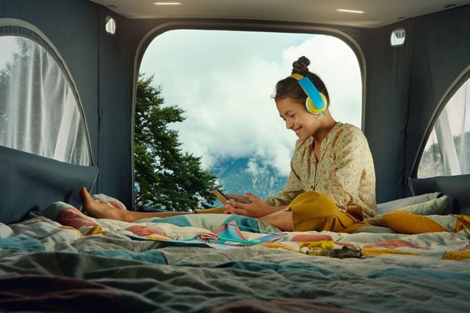 Pessoa sentada na cama alta da autocaravana California 6.1. a ouvir música