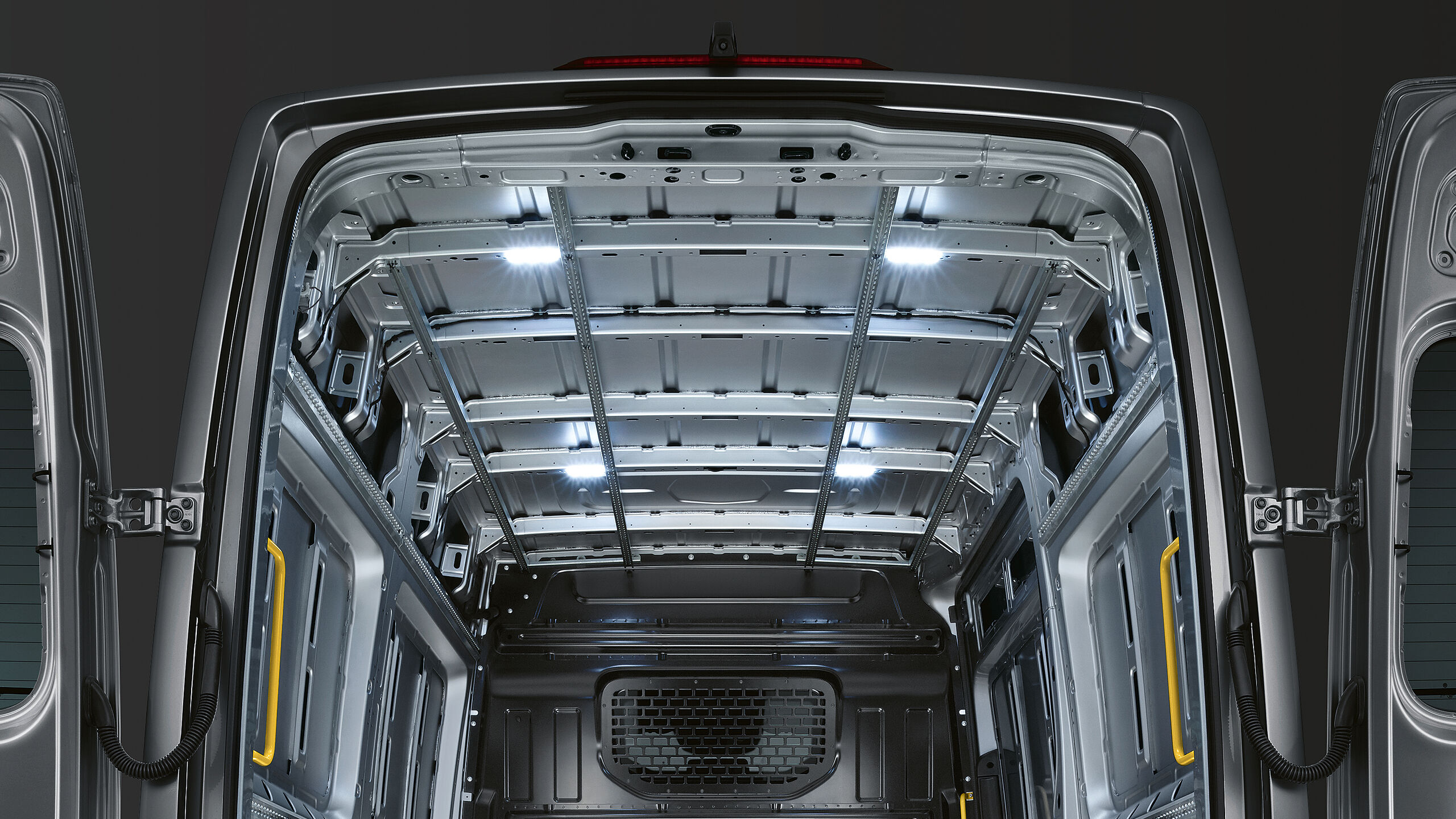 O VW Crafter Cargo parado num espaço escuro. As suas portas traseiras de abertura lateral abertas até trás deixam ver o compartimento de carga vazio.O compartimento da carrinha é iluminado pelos quatro LED montados sob o tejadilho.