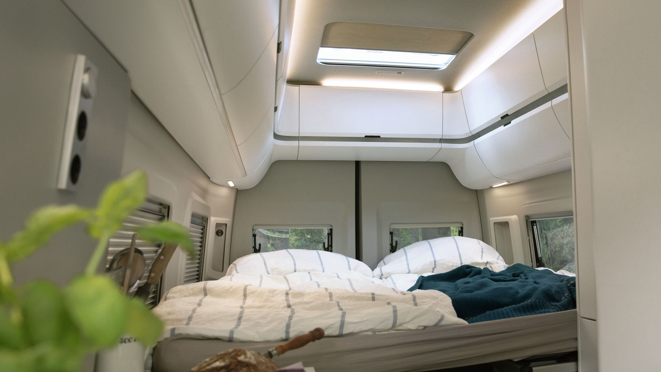 A fotografia mostra a cama na Grand California 680 com iluminação interior acolhedora. 