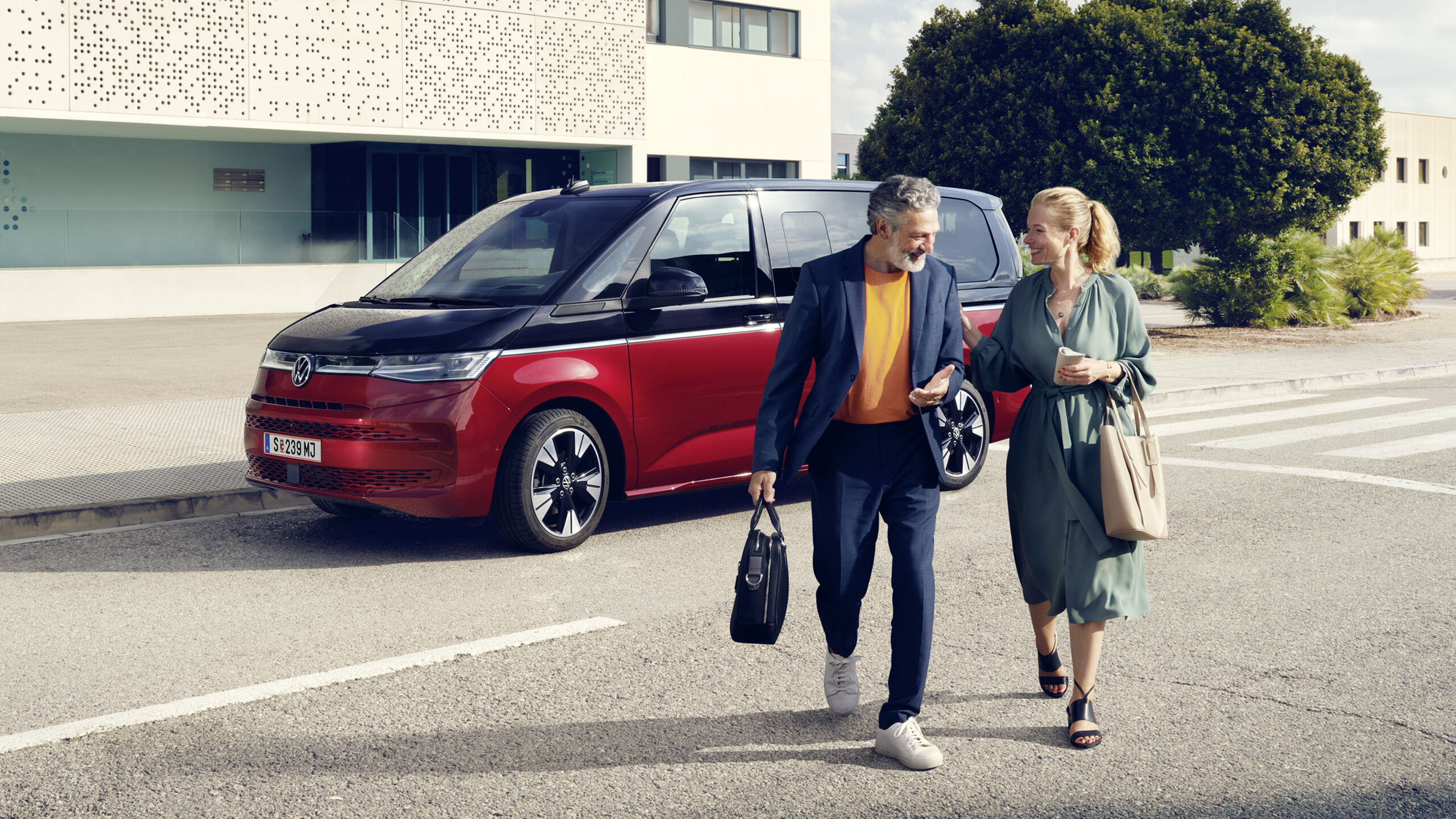 Um homem e uma mulher caminham em frente a uma Multivan VW.