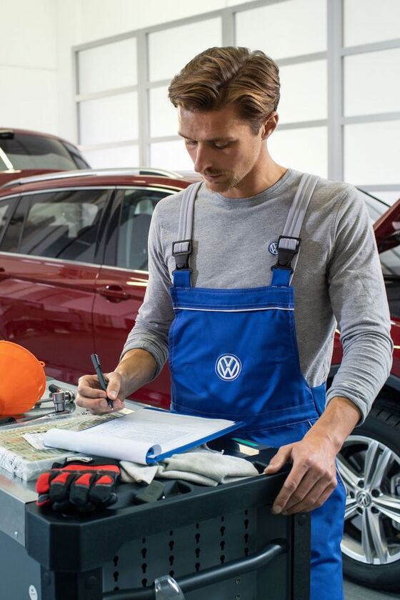 Ein VW Servicemitarbeiter vor einem roten Volkswagen mit Dieselmotor und einer geöffneten Motorhaube in einer Werkstatt