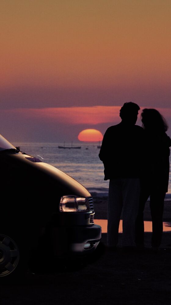 Um casal vê o pôr-do-sol junto à sua VW California