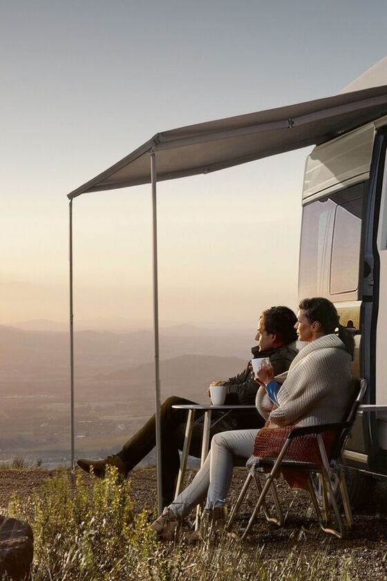 Um casal sentado à frente da Grand California a contemplar o nascer do sol