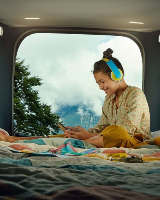 Pessoa sentada na cama alta da autocaravana California 6.1. a ouvir música