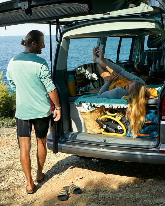 A porta traseira aberta da VW California 6.1 Beach com um casal a conversar.