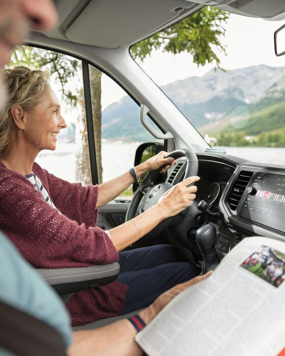 Cockpit de uma Grande Califórnia. Uma mulher está sentada ao volante, o homem ao seu lado está a ler um jornal.